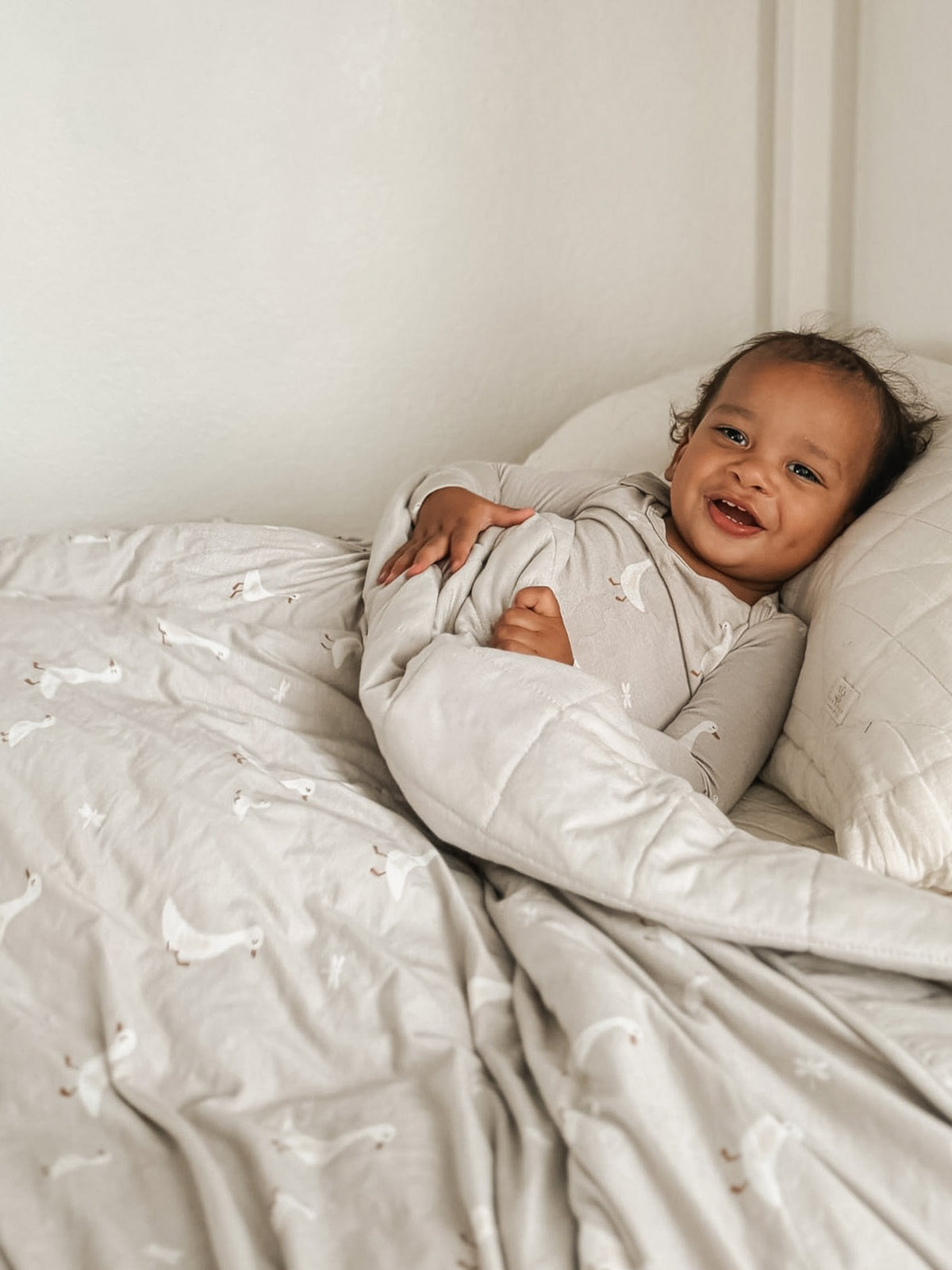Goose print blanket in light gray, partially covering a child on a bed.