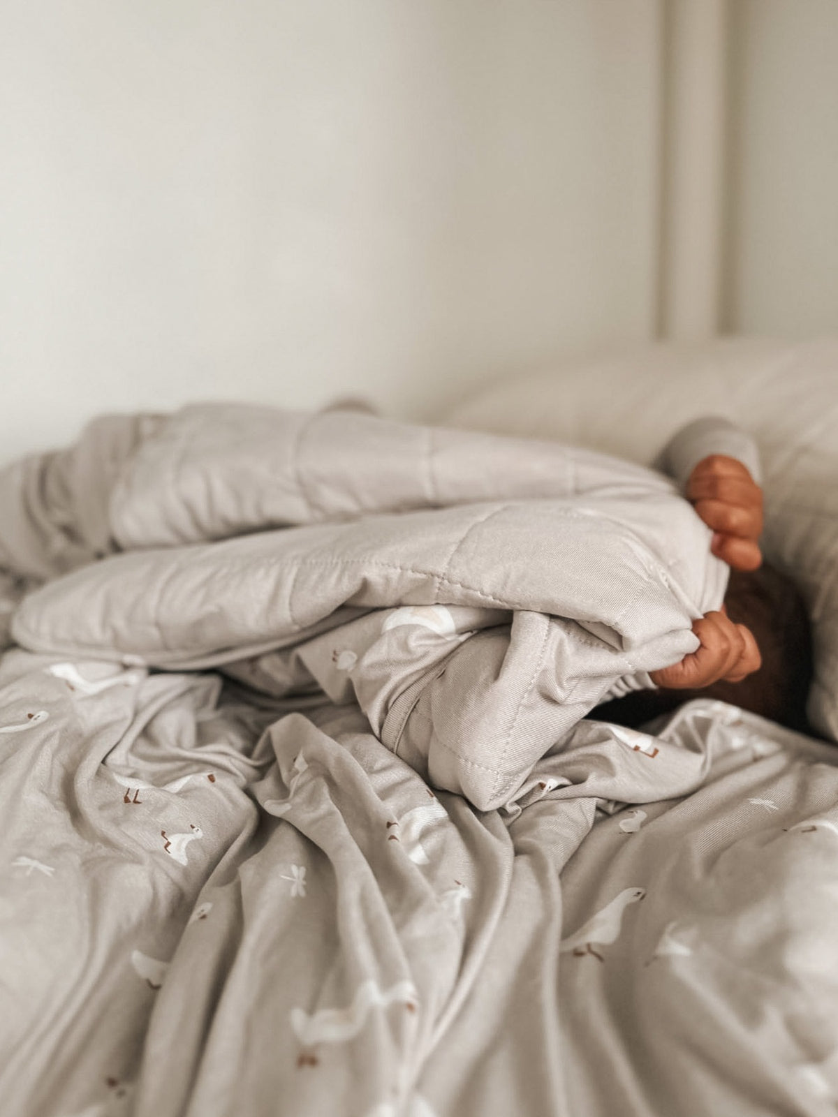 Light gray blanket with white goose motifs, loosely layered and bunched on bed.
