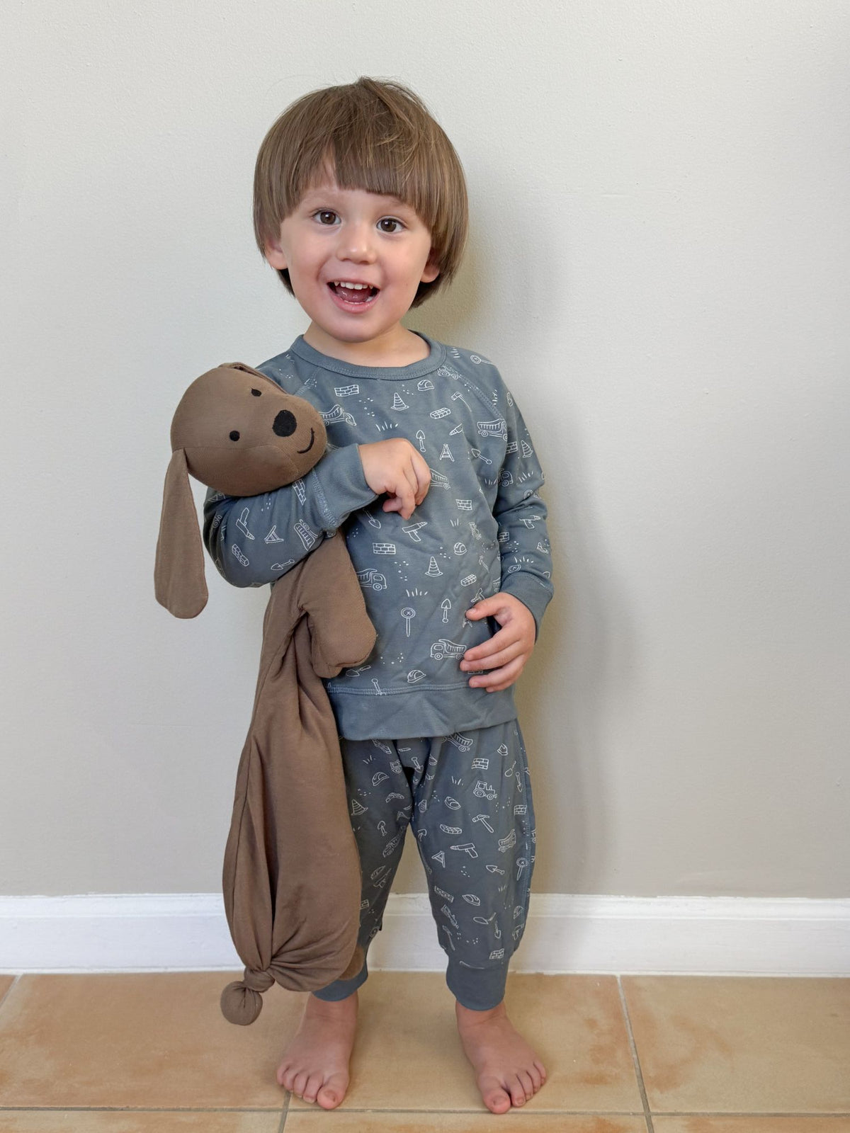 Plush dog lovey with stitched face and floppy ears, baby holding it at chest.