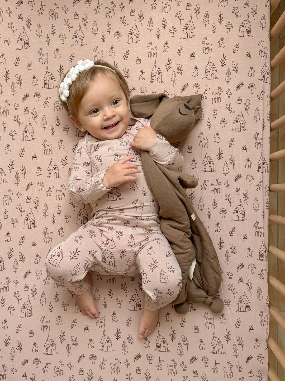 Plush peanut dog lovey with floppy ears and stitched face, draped over baby's arm.