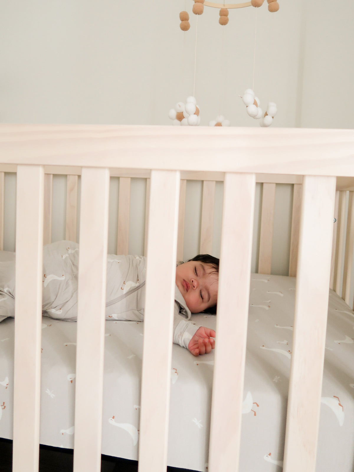 Taupe crib sheet with all-over white goose motif behind crib rails