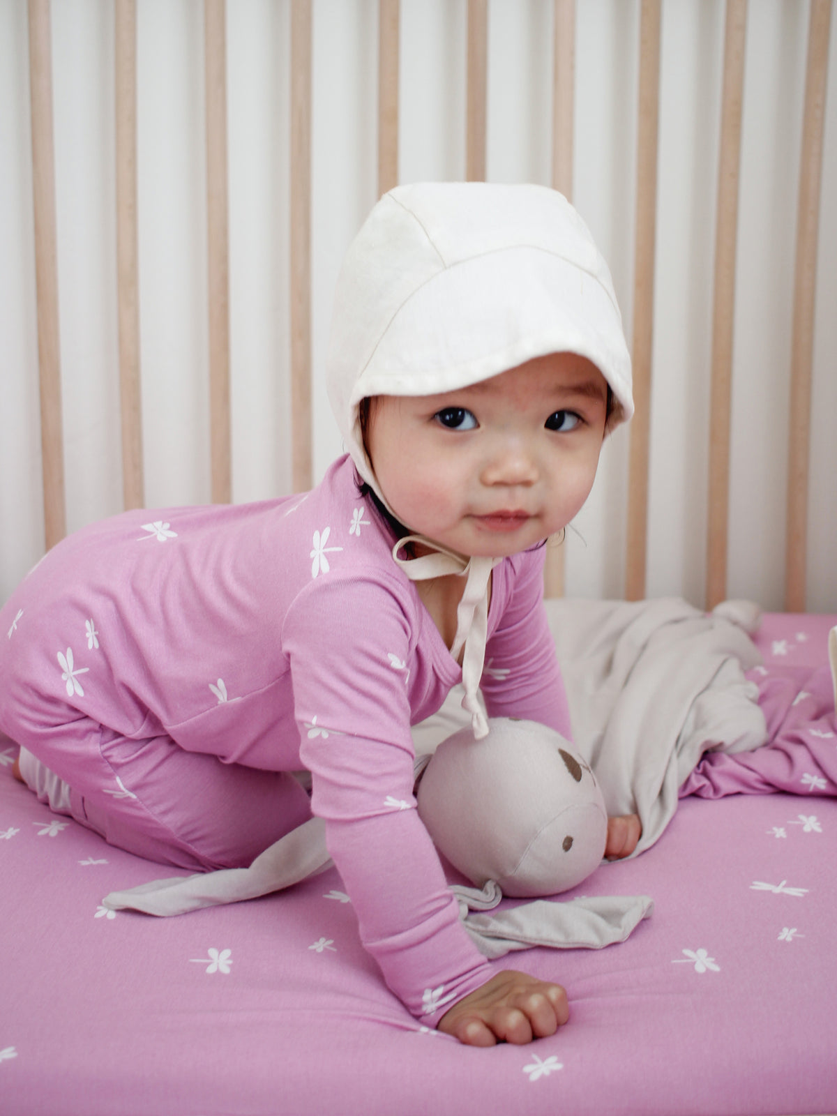 Pink hooded pajama with firefly print, baby lying on bed holding plush bunny