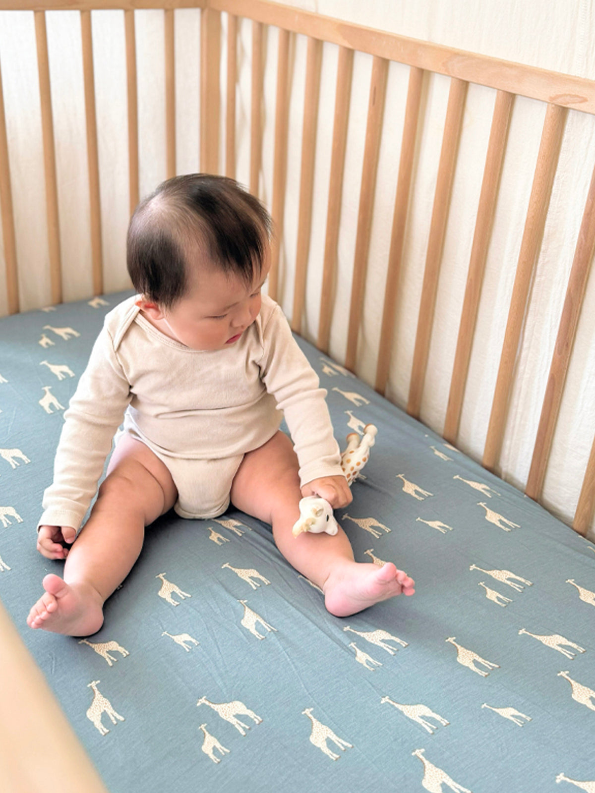 Crib sheet on crib with teal background and beige giraffe print, baby sitting