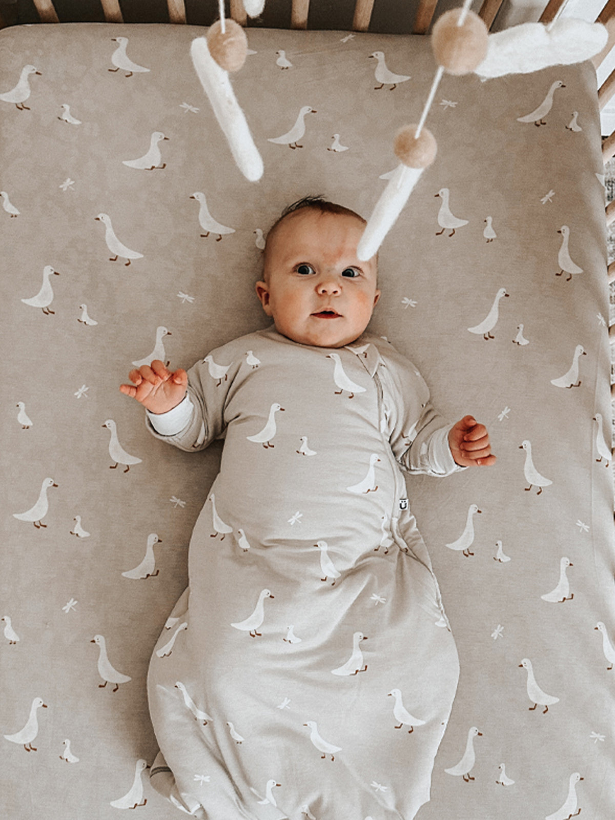 Taupe crib sheet with repeating white goose print and subtle gold accents