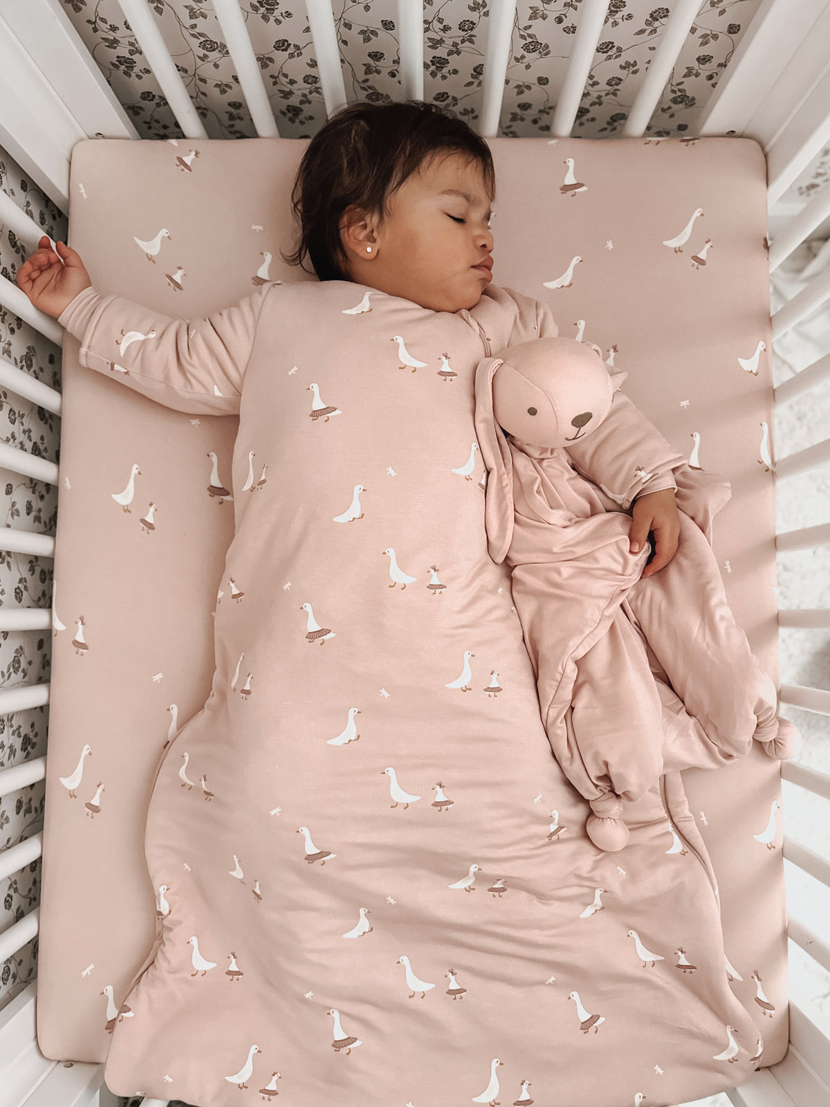 Pale pink bunny lovey blanket with white bird print and small plush bunny, shown on crib