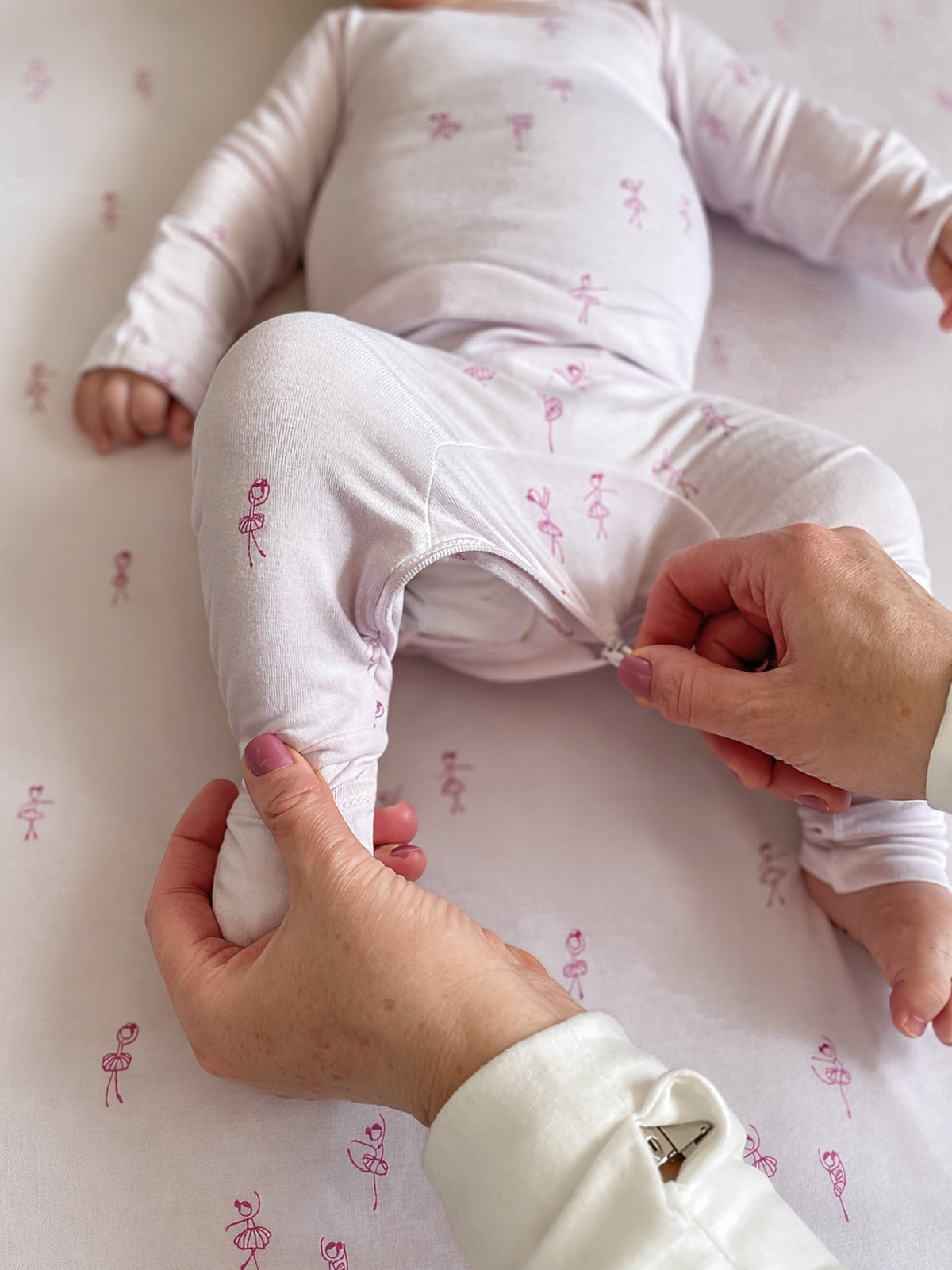 Light pink baby convertible pajama with ballet print, leg opening detail being adjusted
