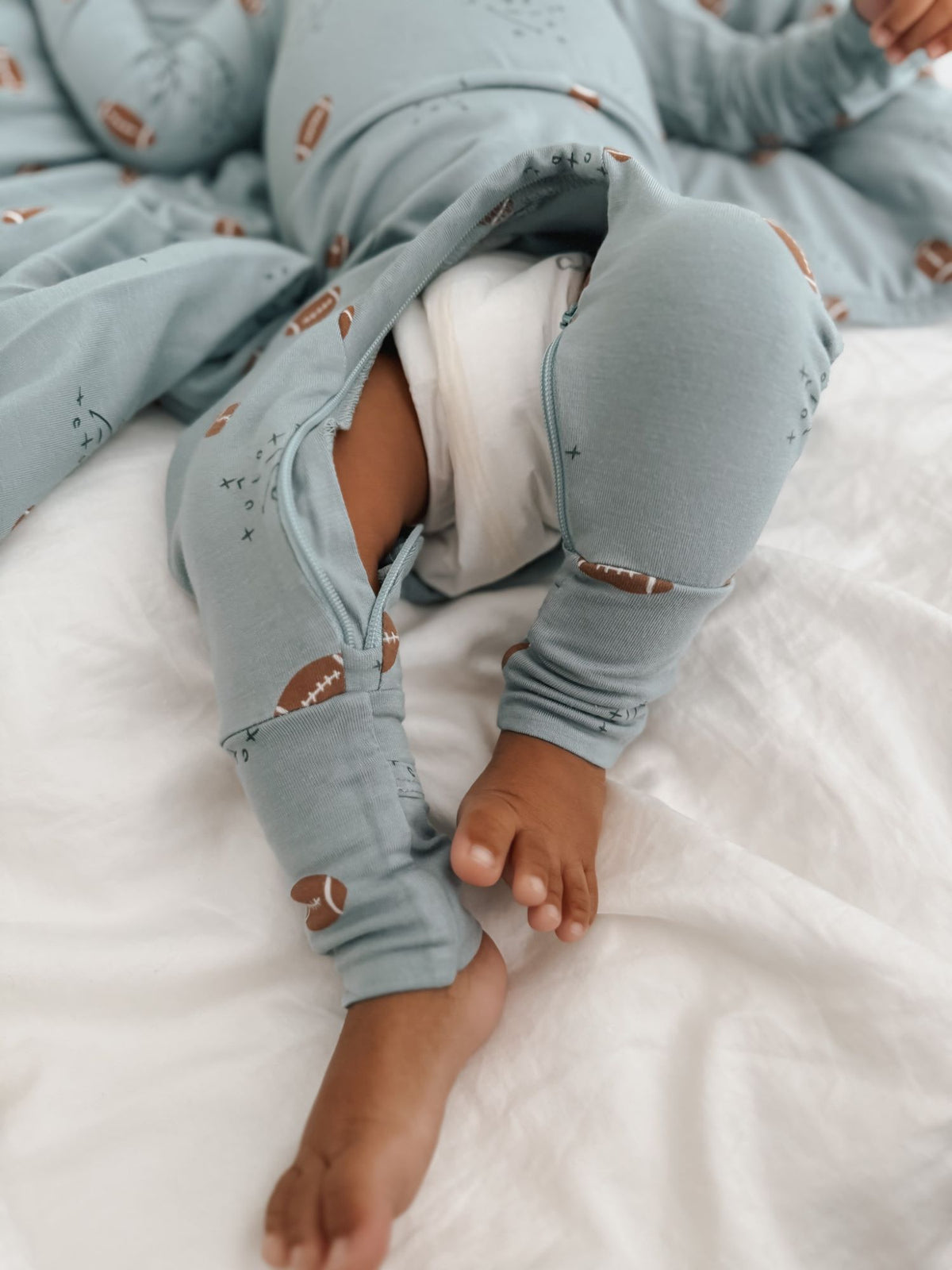 Light blue baby footie pajamas with football print, side view showing covered feet