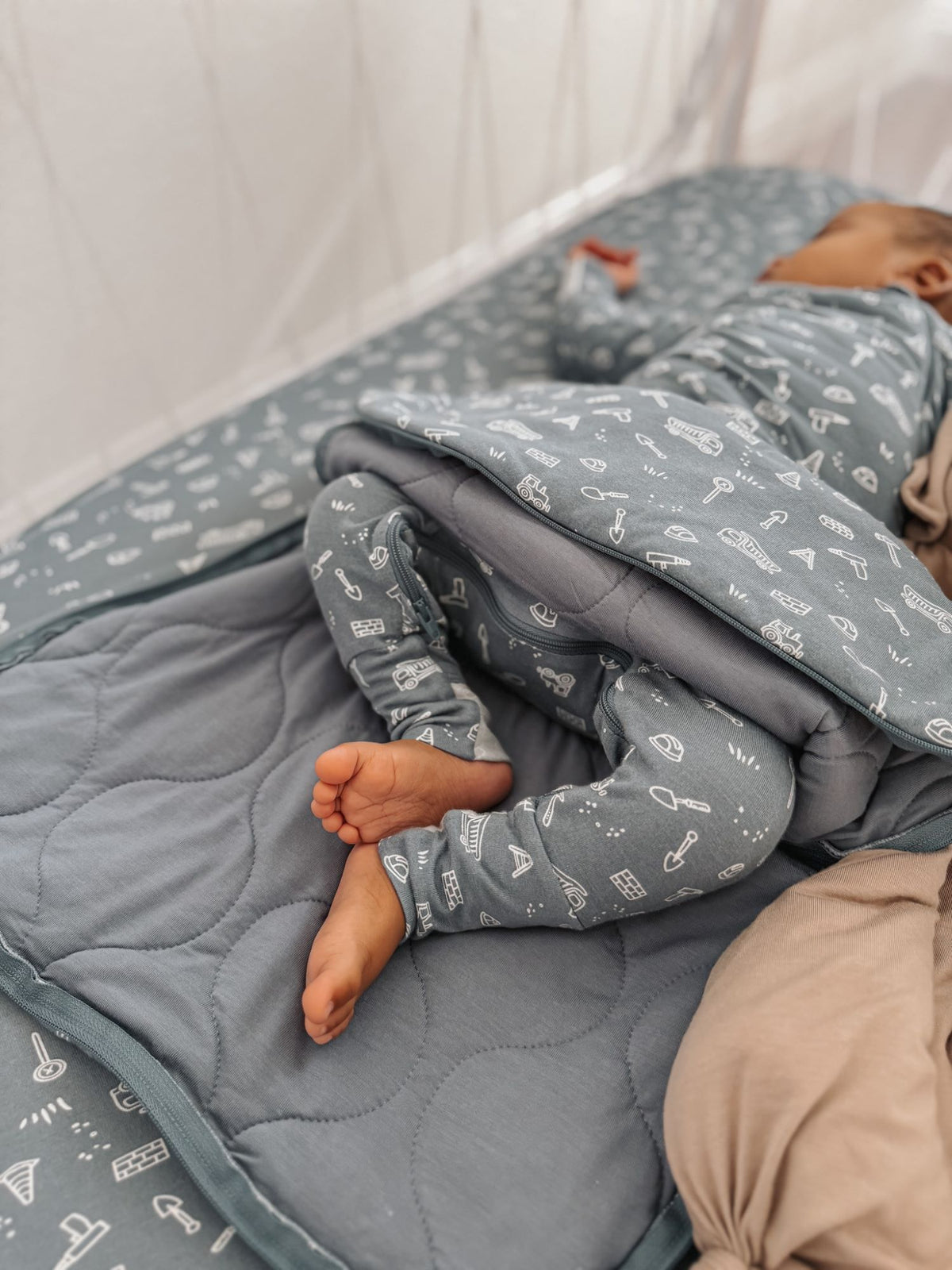 Long-sleeve swaddle sack in blue-gray with white icons, baby tucked in