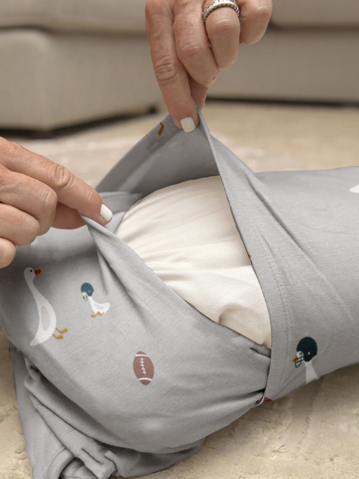Gray nap mat with goose and football prints, hands adjusting top flap and strap