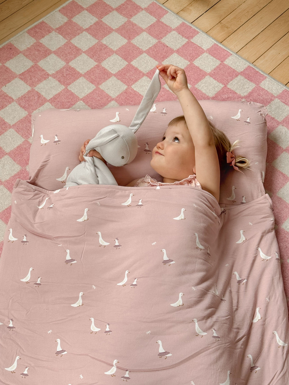 Light pink nap mat with white goose pattern, baby lying back with arms up