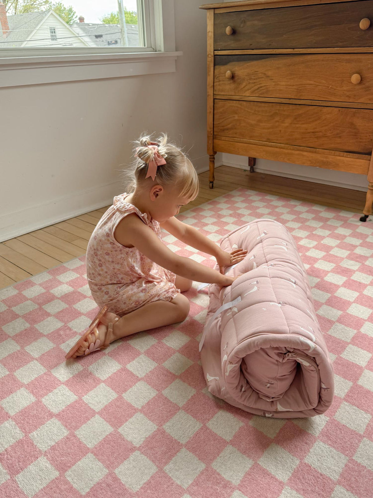 Light pink nap mat with white goose pattern, baby sitting beside the rolled mat