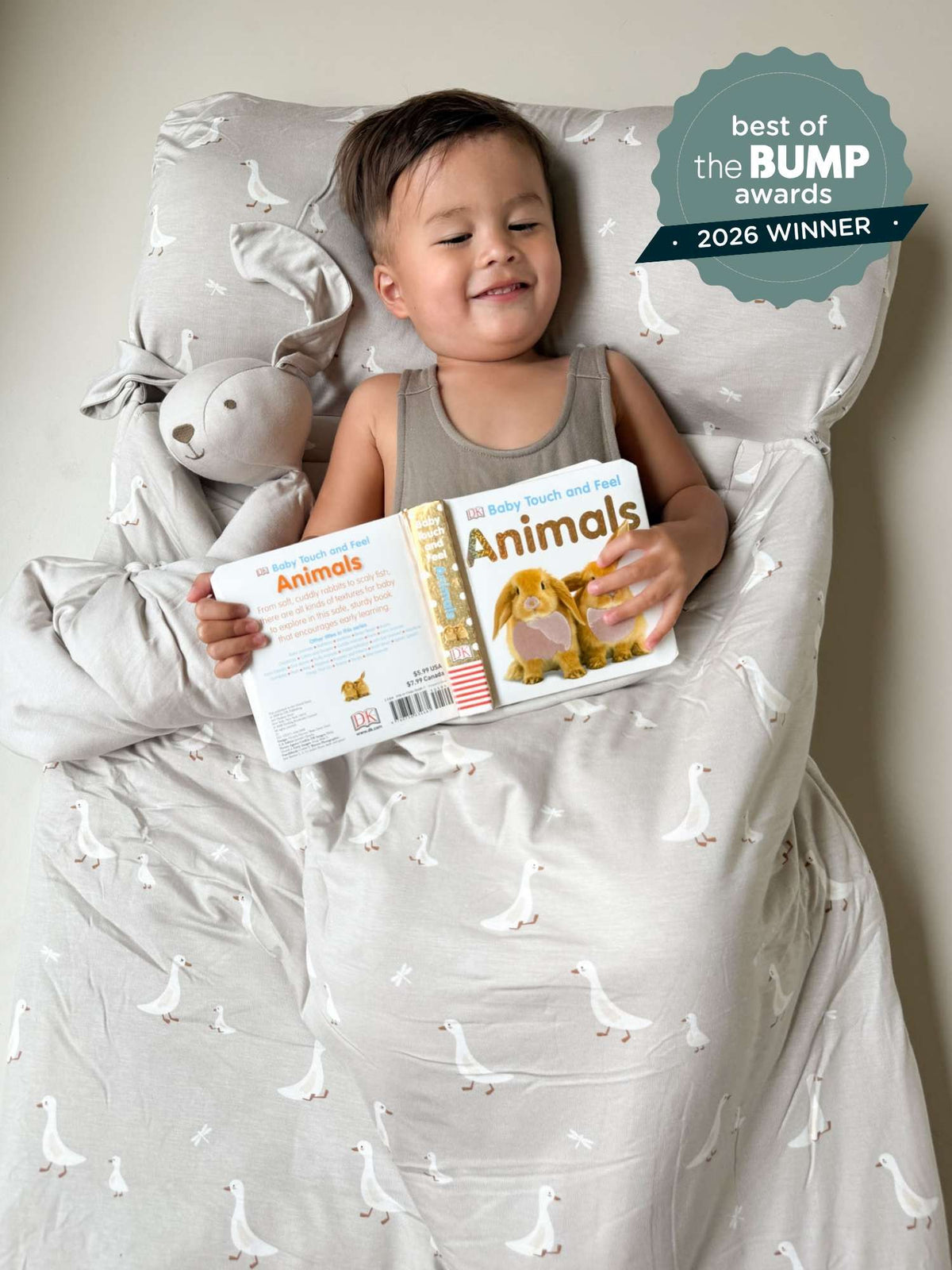 Goose-pattern nap mat on bed, baby seated and holding a book; white geese print