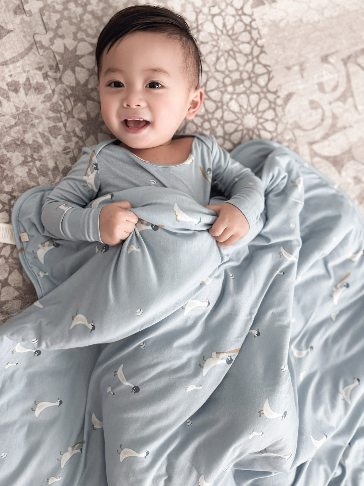 Light blue goose-print baby blanket wrapped around toddler on bedding