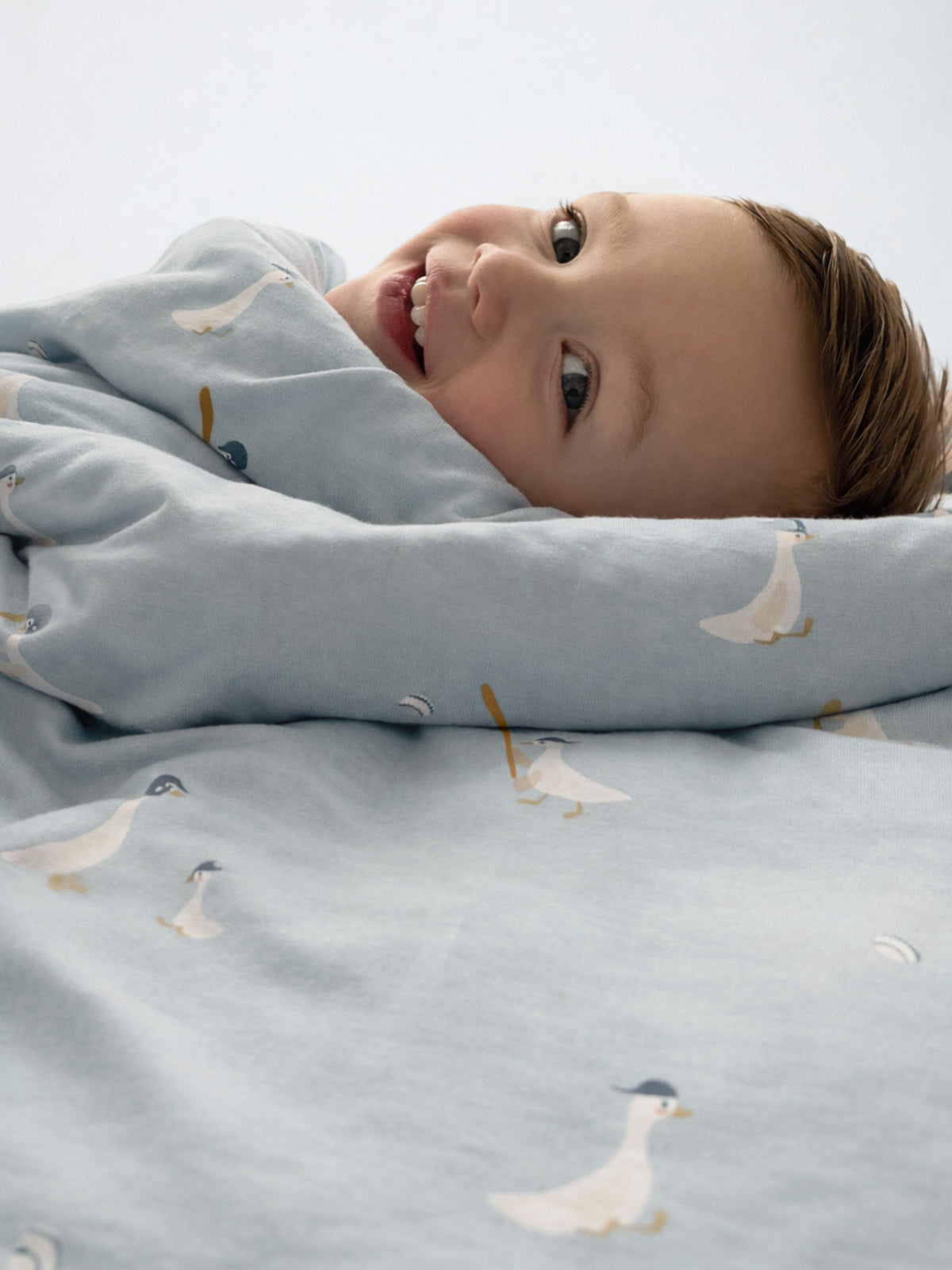 Light blue baby blanket with white goose pattern, tucked under resting head