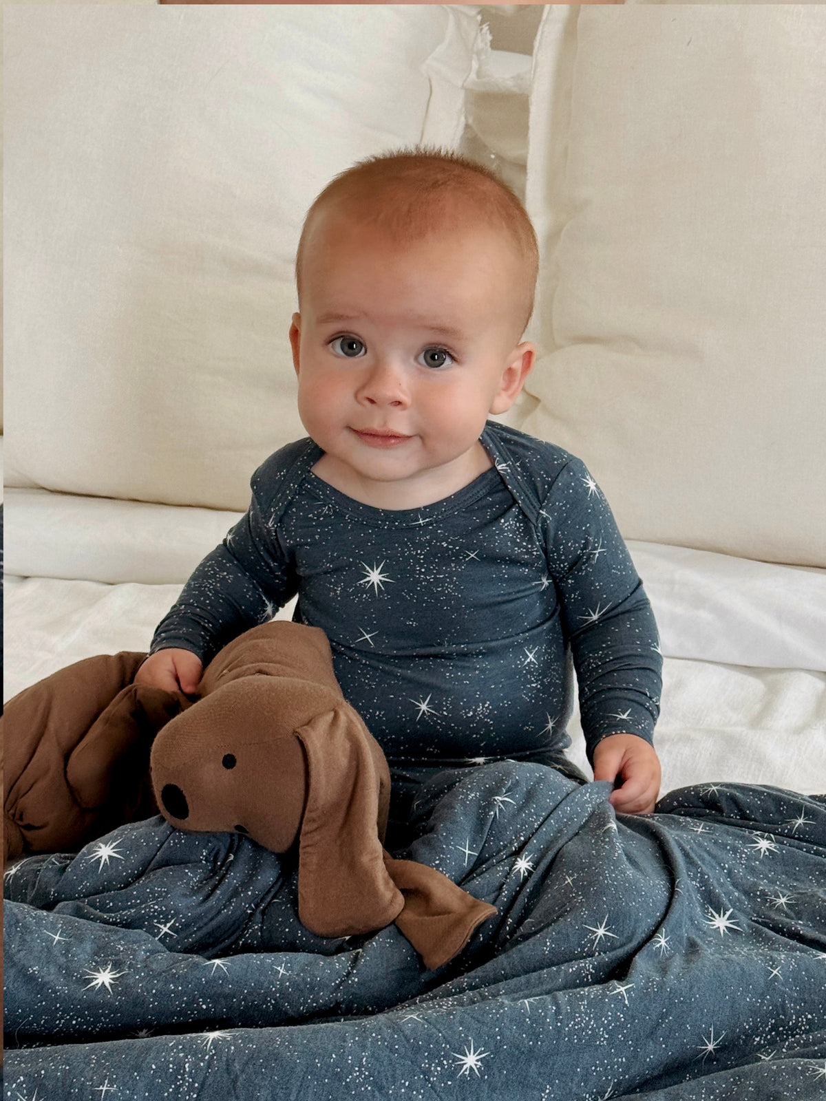 Plush peanut dog lovey with floppy ears and stitched face, held in baby's arms.