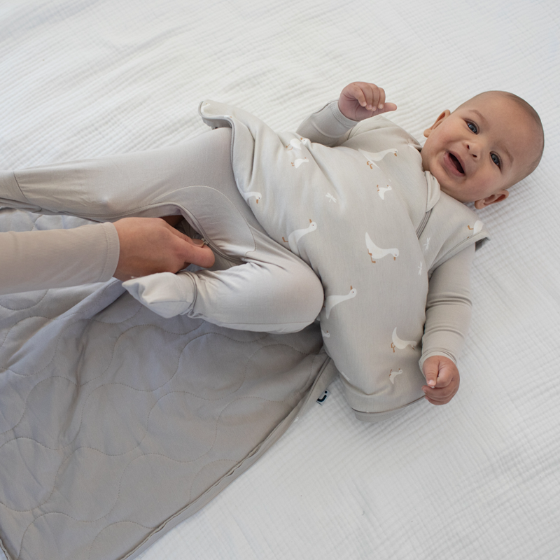 Light gray baby sleep sack with white duck print, worn over long-sleeve bodysuit
