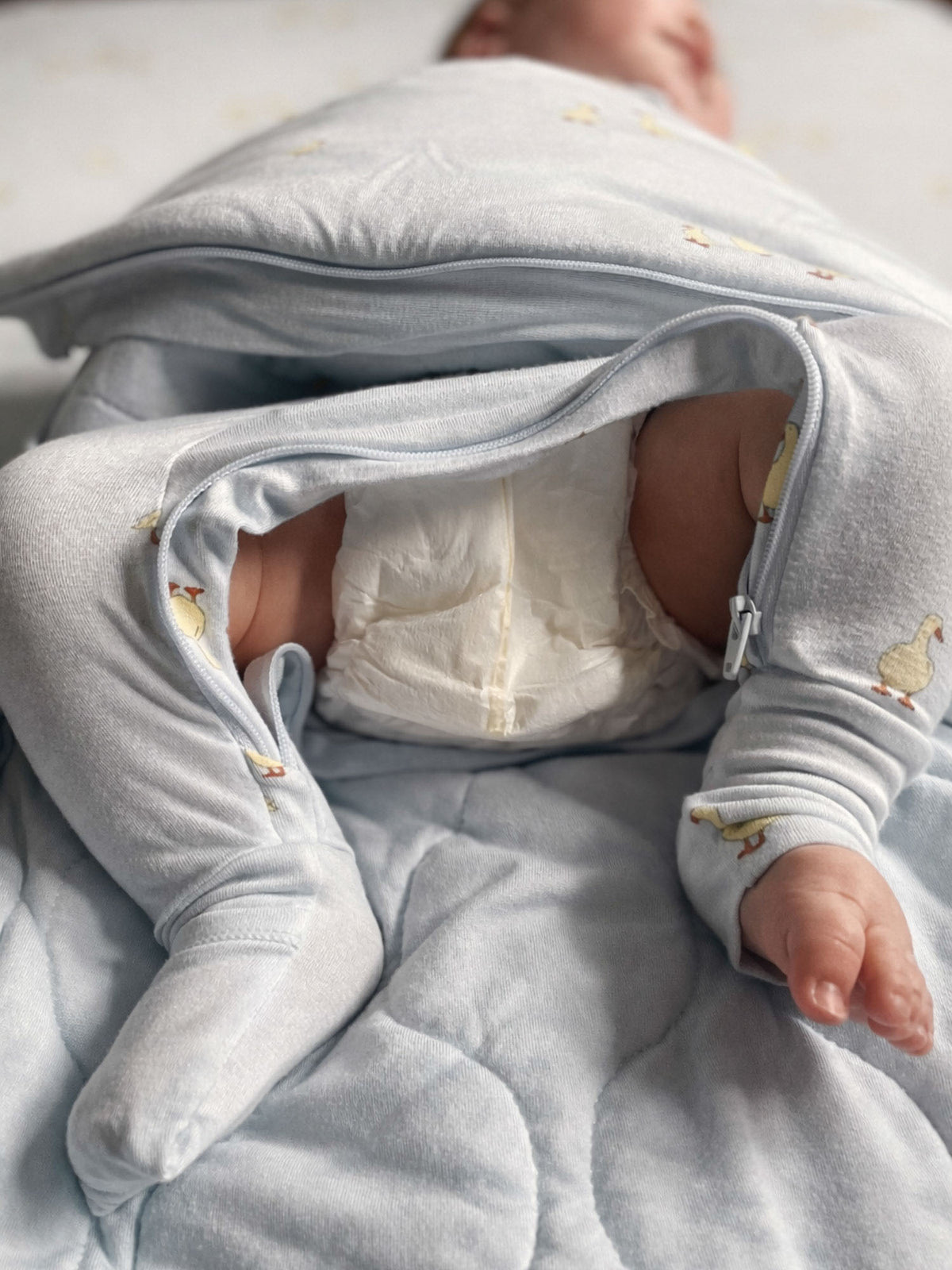 Light gray swaddle sleep sack with yellow animal prints, open zipper and padded interior