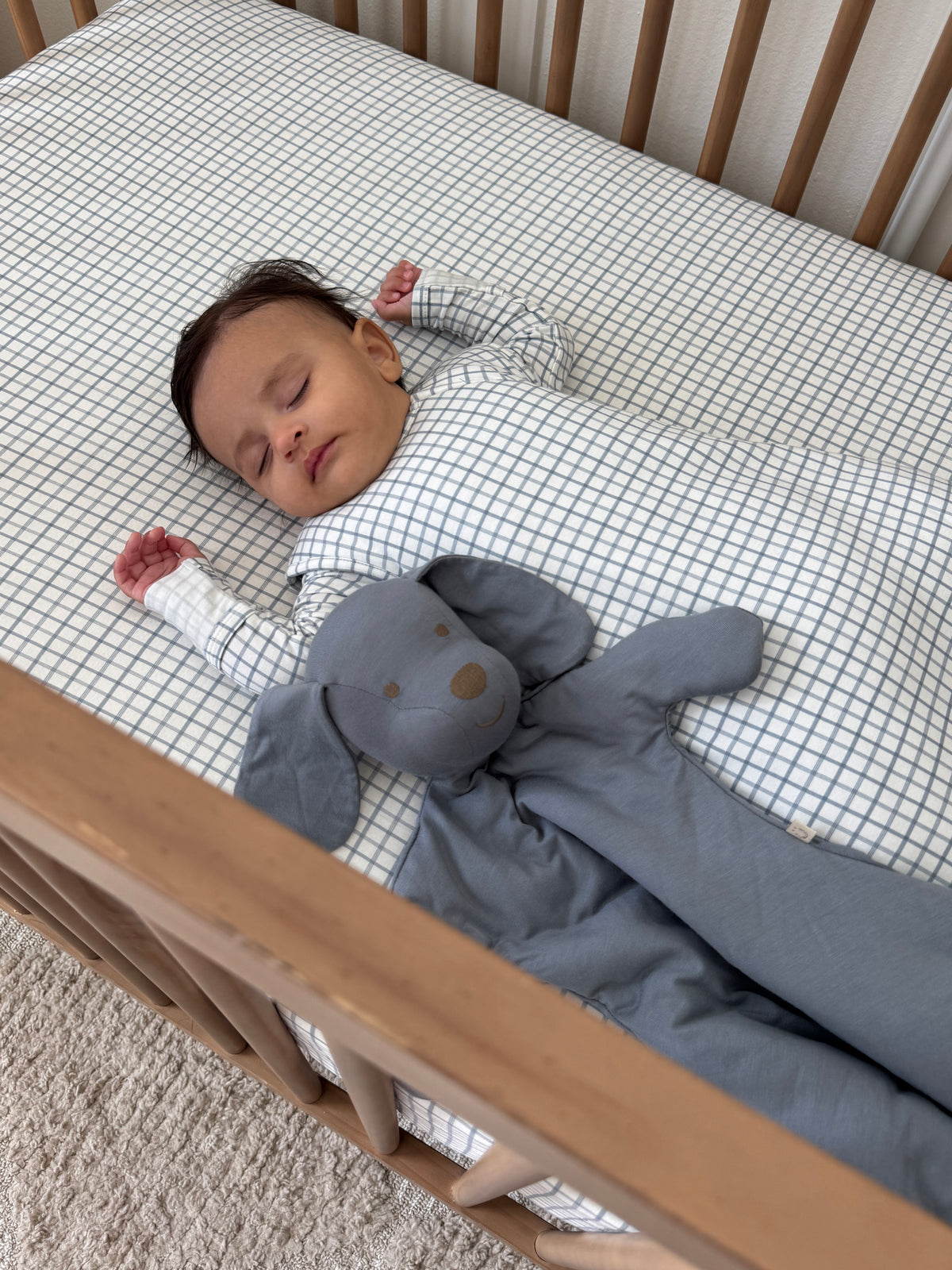 Checkered transitional swaddle sleep sack with gray bottom, baby lying on crib