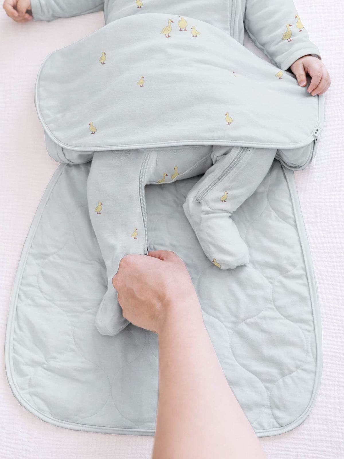 Light blue swaddle sack with long sleeves and folded legs, character print detail.