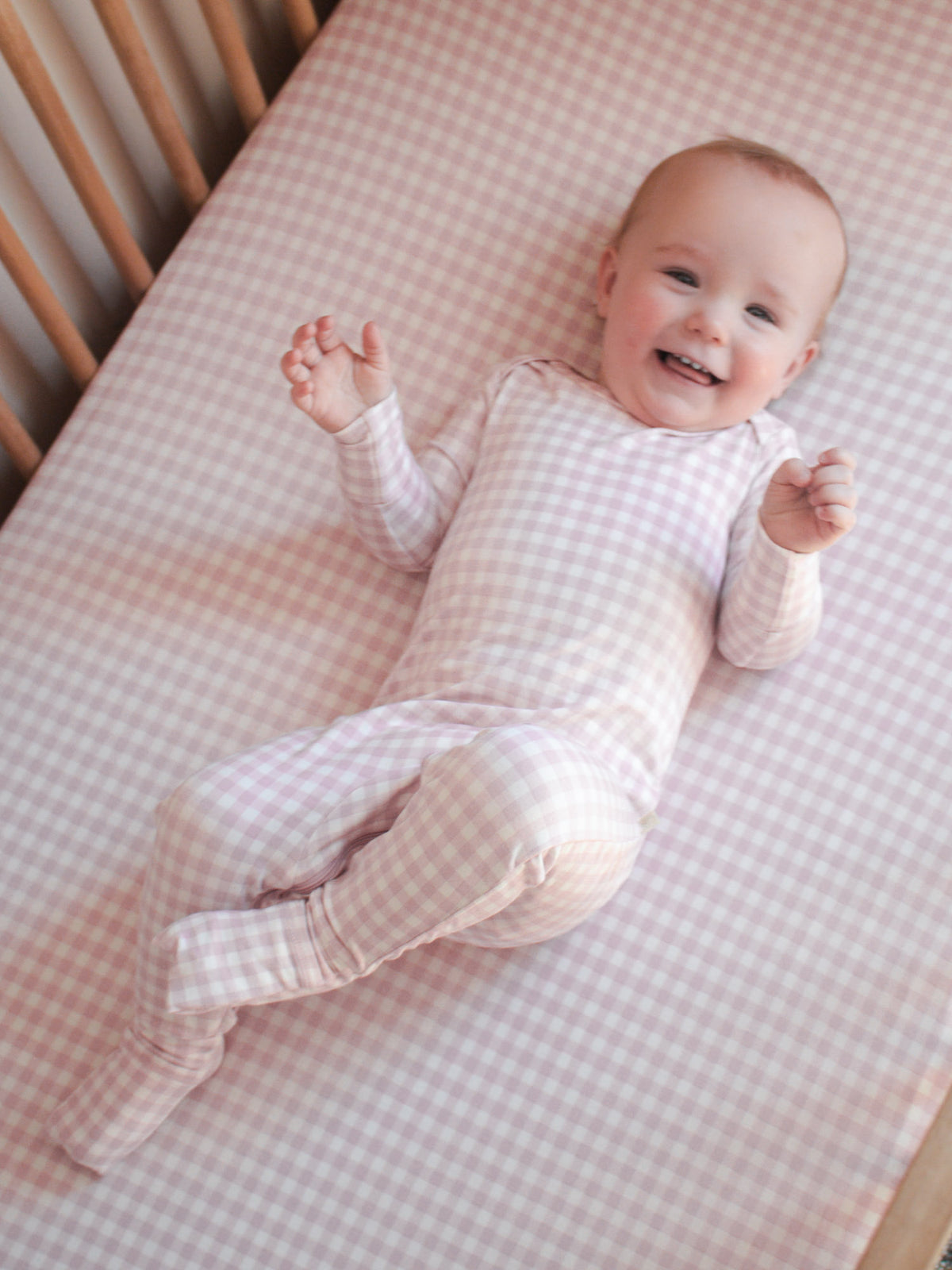 Pink gingham long-sleeve pajama set on baby with footed legs and elastic cuffs