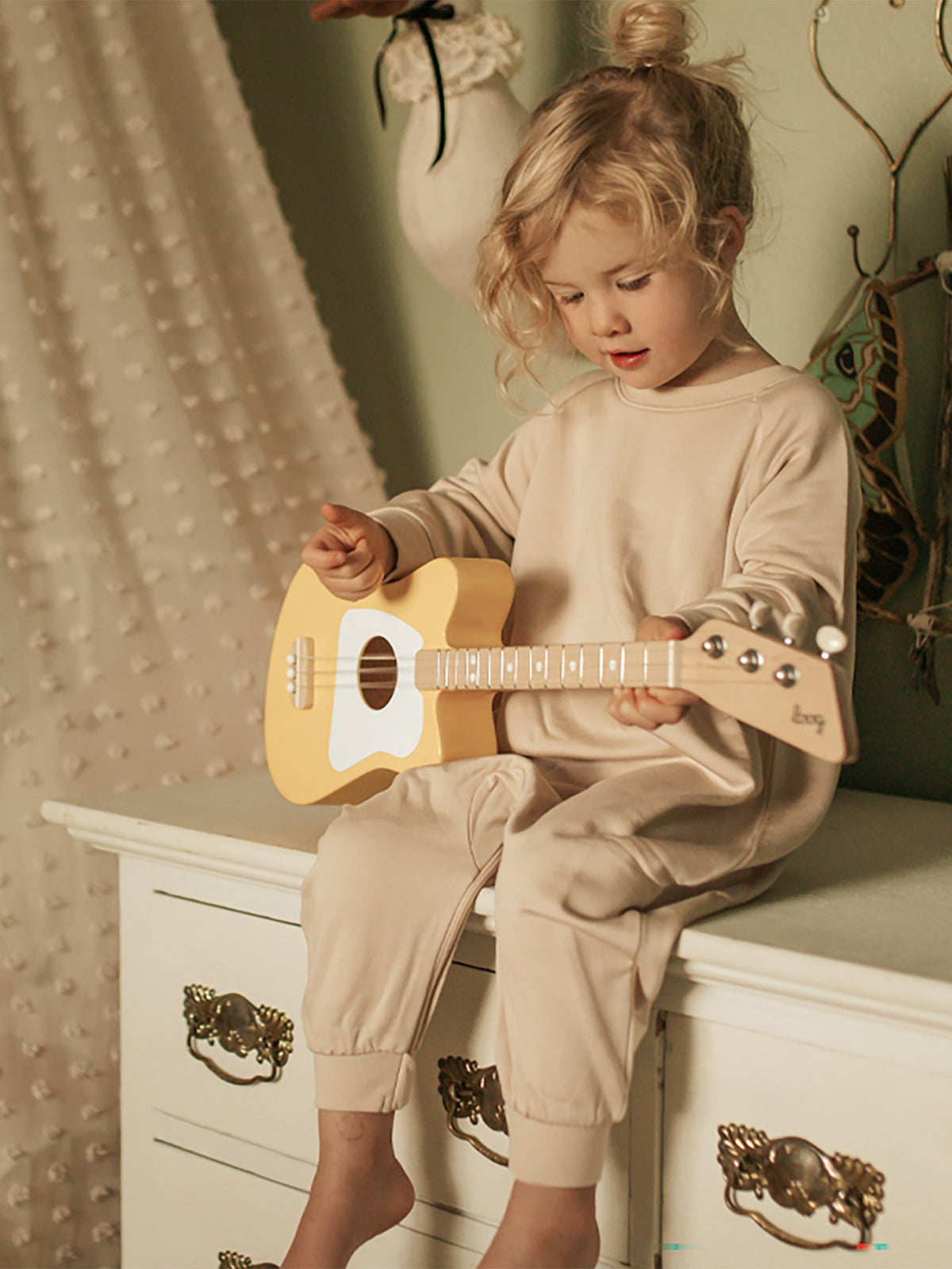 Light blush fleece baby jumpsuit with long sleeves, worn while holding toy guitar