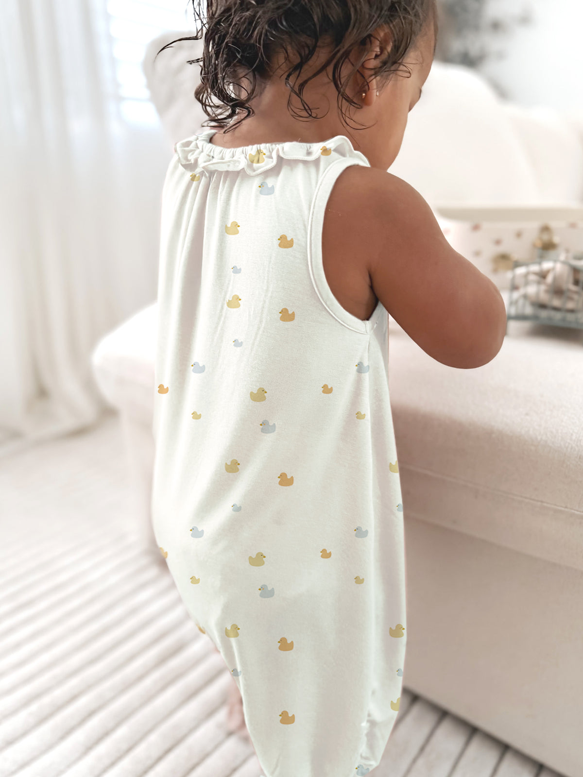 Cream duck-print sleeveless romper with ruffled neckline and gathered legs