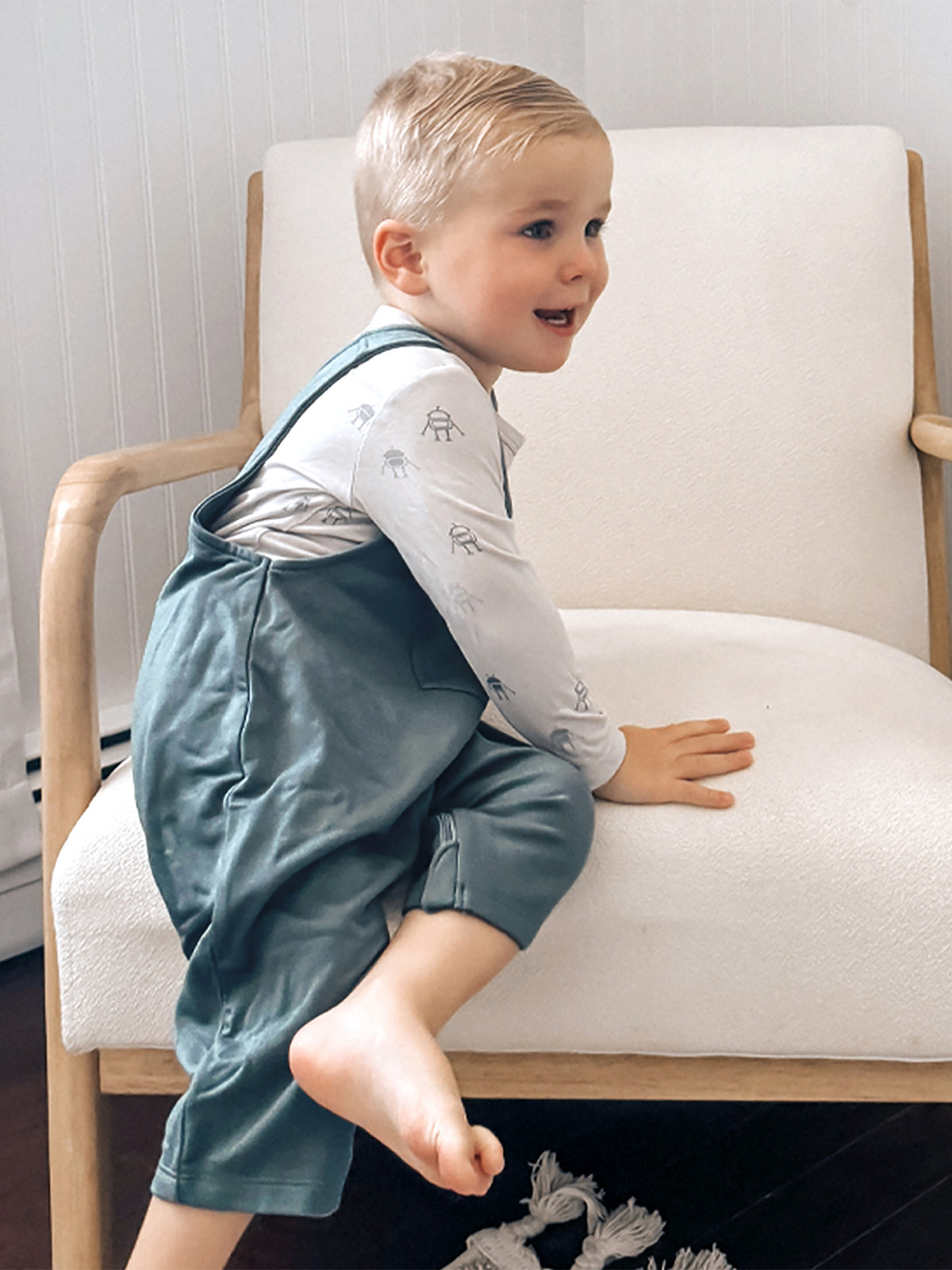 Teal fleece baby overalls with front pocket, worn over long-sleeve shirt