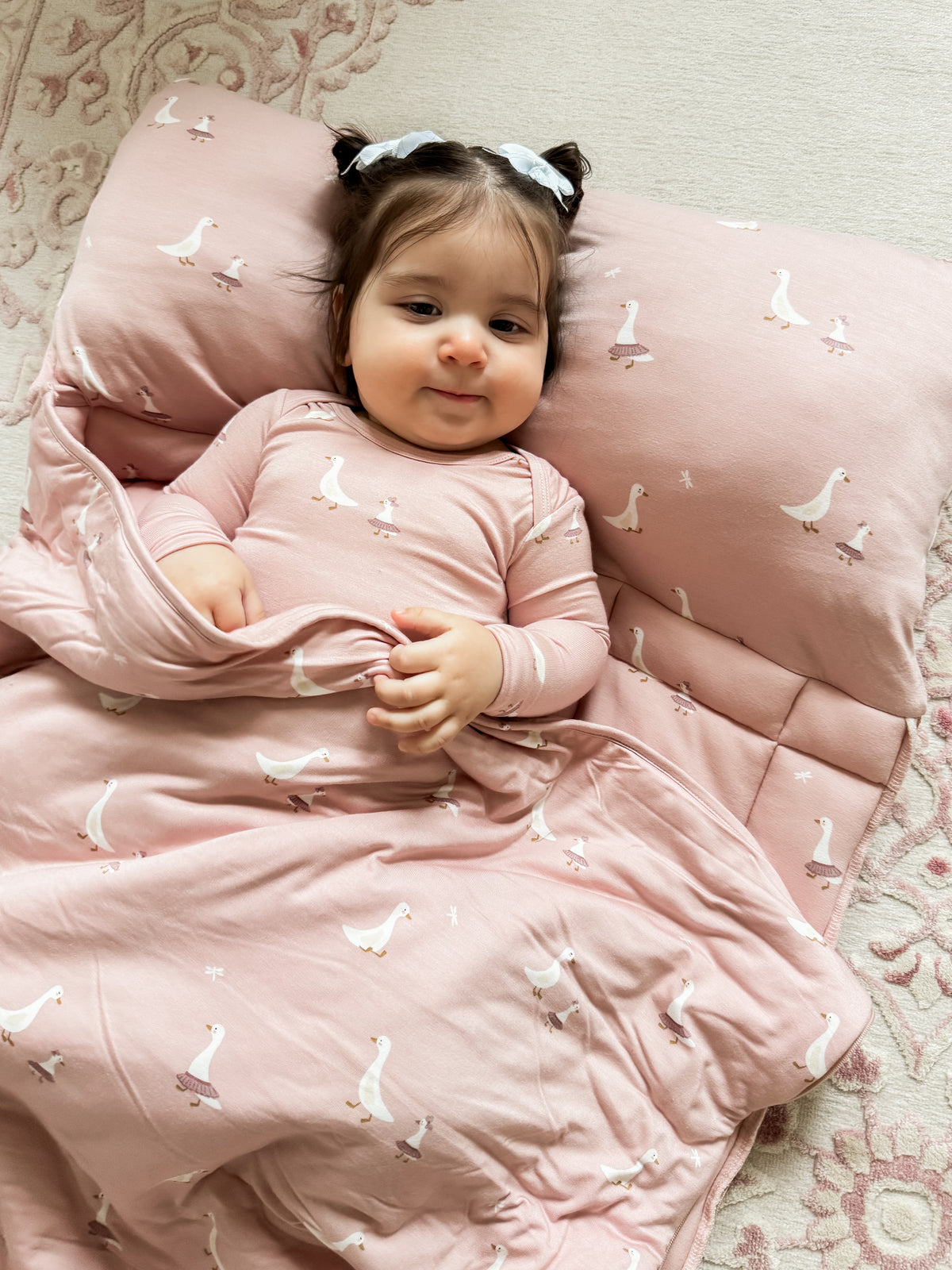 Light pink nap mat with white goose pattern, cushioned headrest and baby lying