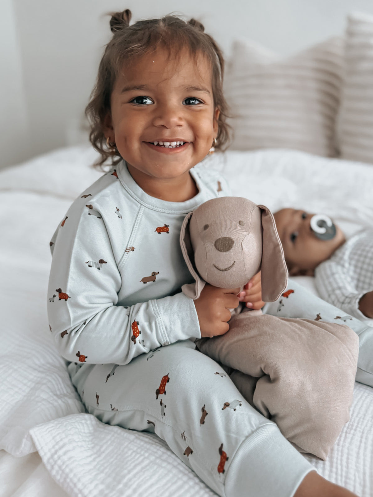 Light blue pajama set with taupe puppy plush lovey held close by baby.