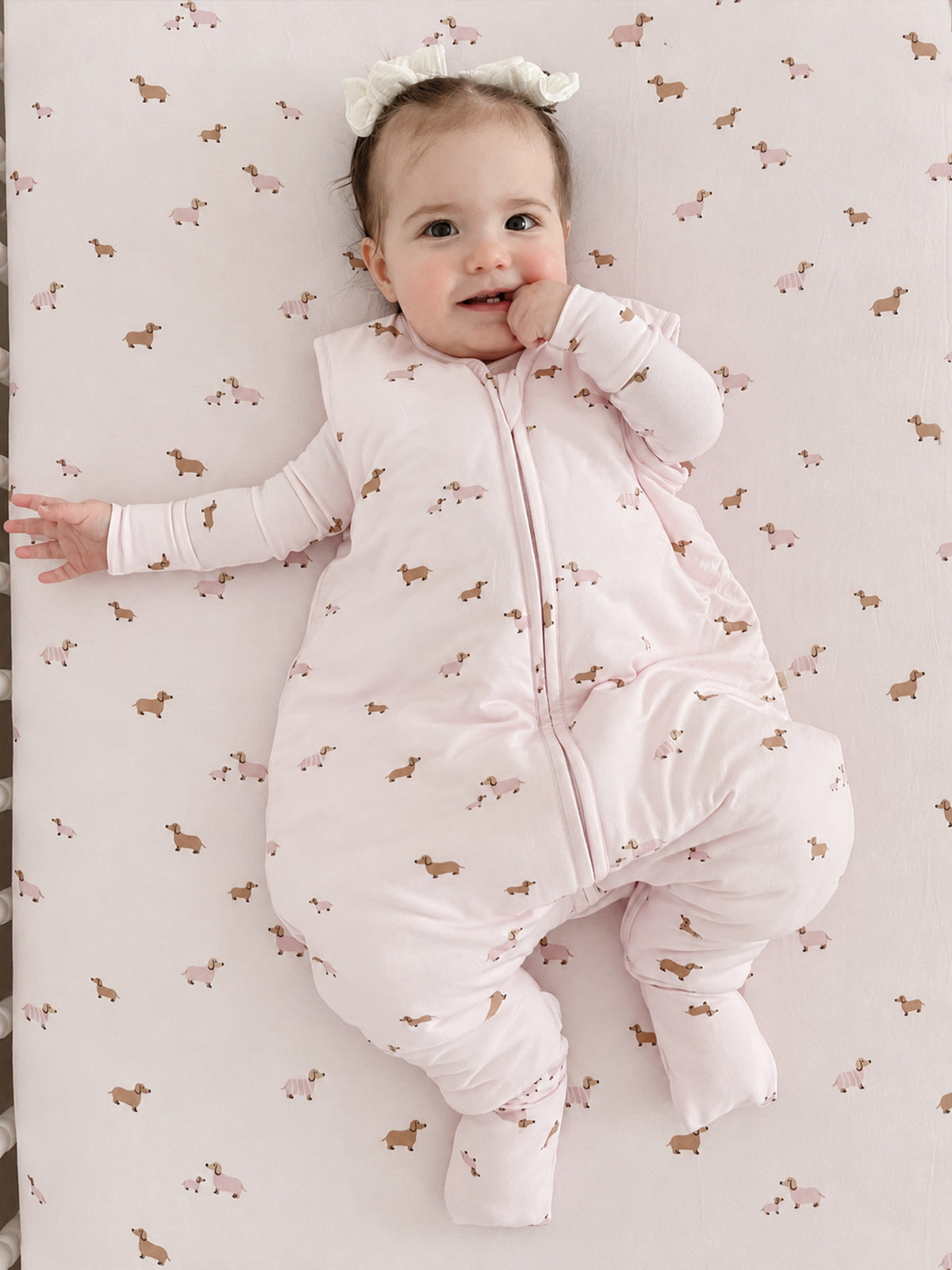 Crib sheet with scattered dog print in pink and tan on a light background