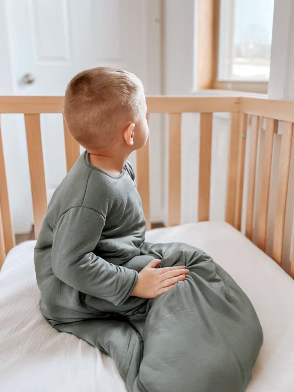 Sage green long-sleeve sleep sack with front zipper, child sitting sideways