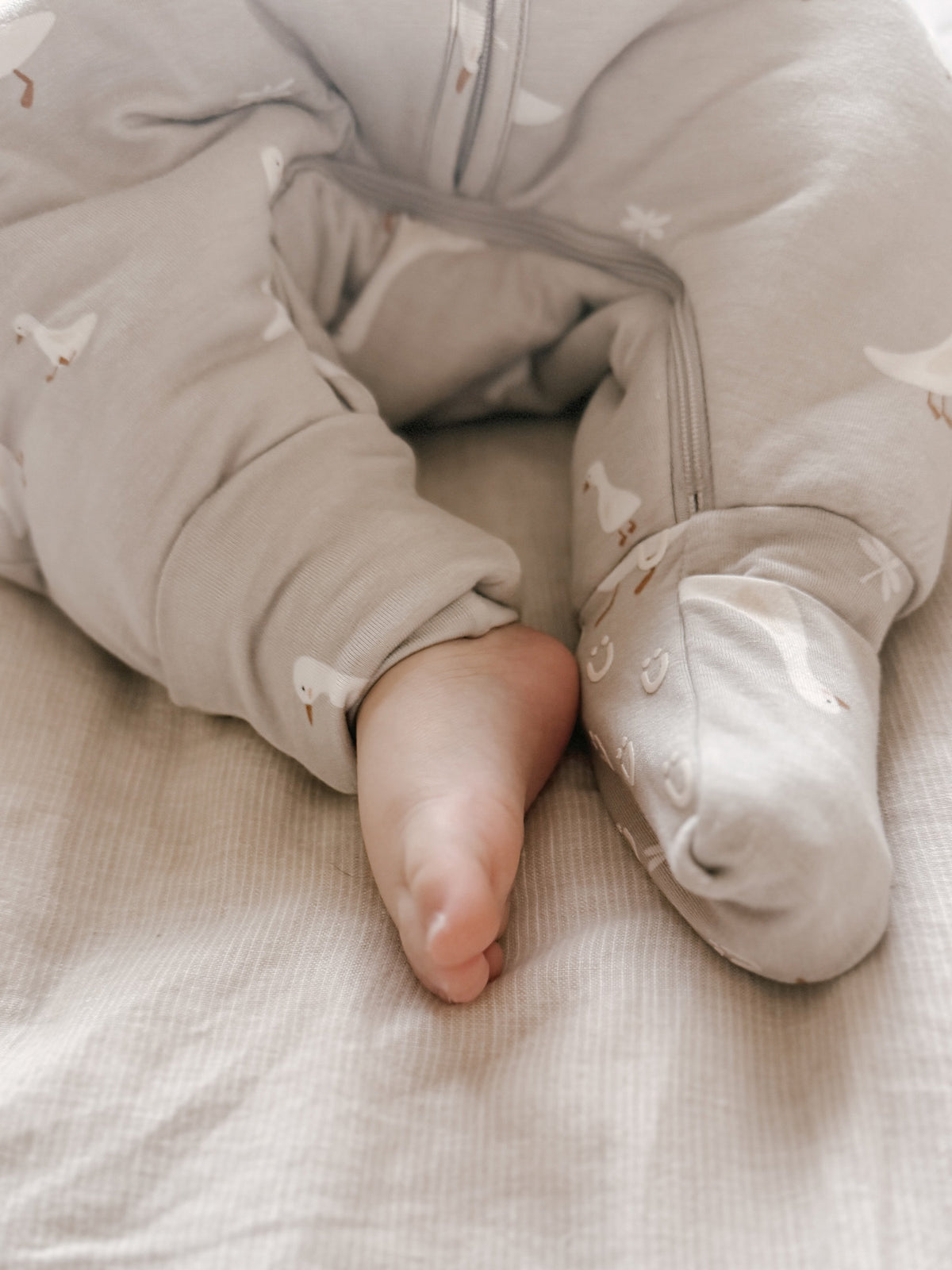 Footie sleep sack close-up with goose print cuffs, zipper front, and visible baby feet