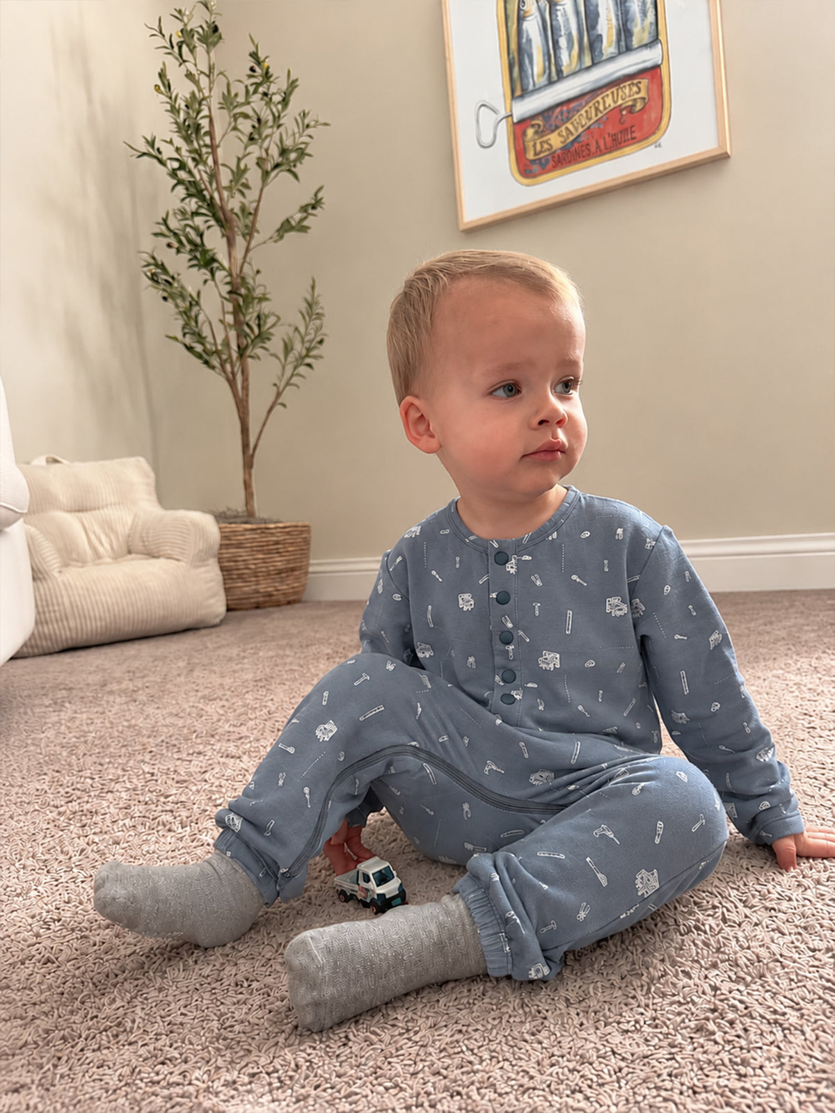Blue tool-print henley jumpsuit with button-front and long sleeves, seated