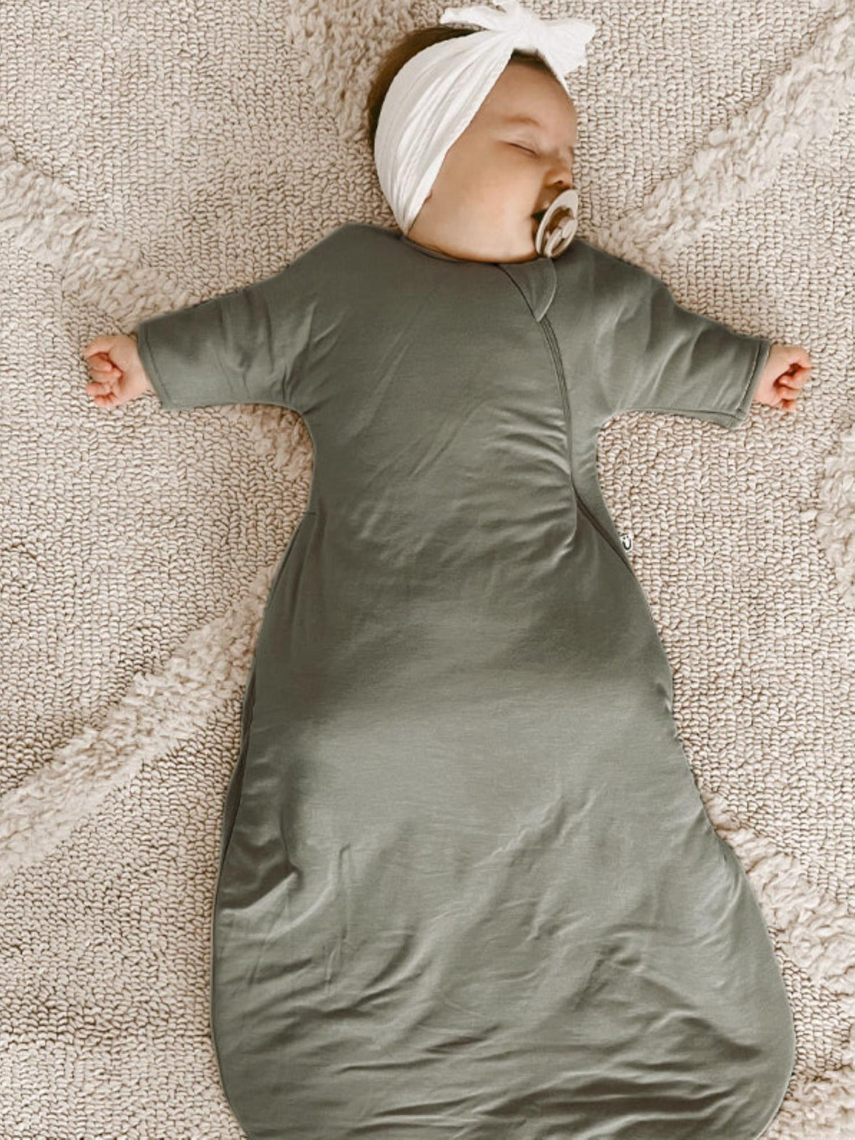 Sage green long sleeve swaddle sack with front zip, baby lying on textured fabric