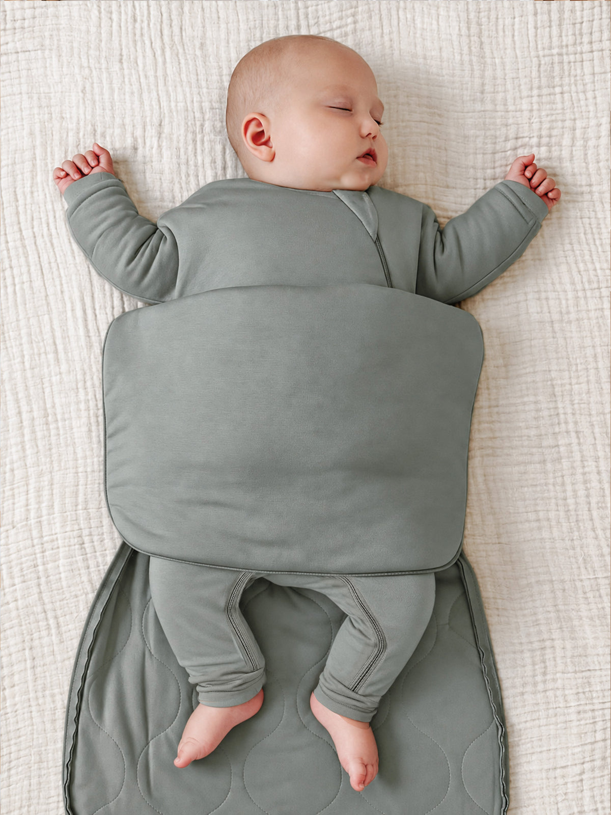 Sage green swaddle sack with folded lap flap and leg openings, baby lying back