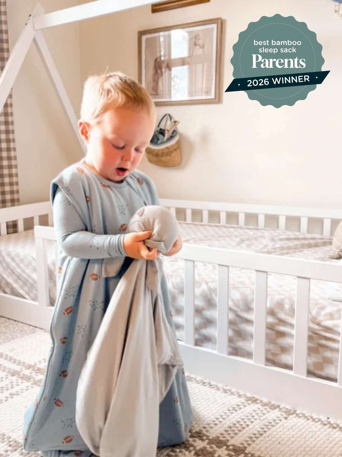 Blue football-print sleep sack with long sleeves and zipper, toddler holding the fabric up
