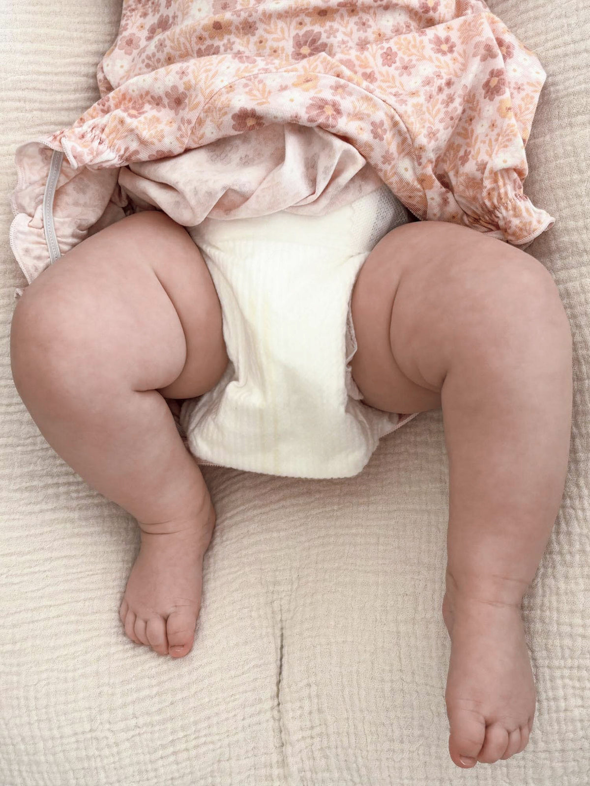 Peach-pink floral bubble romper with ruffled neckline, open leg design view