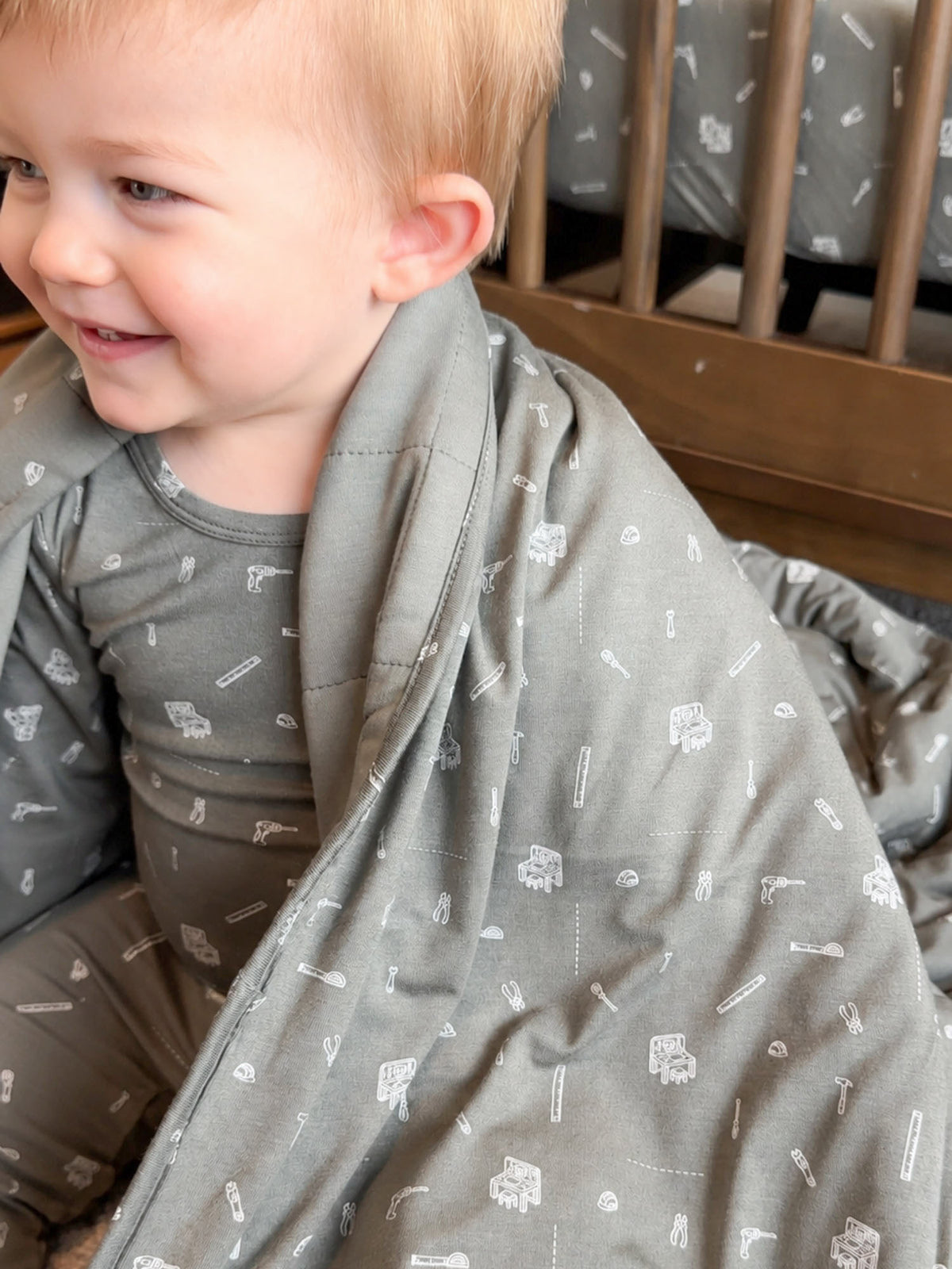 Twin-size gray blanket with small tool pattern, draped over child in crib