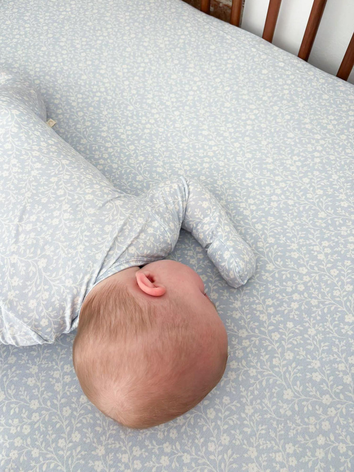Light blue crib sheet with white floral sprig print, fitted around baby on the mattress