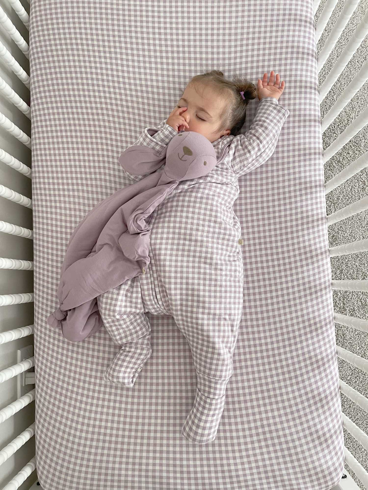 Crib sheet with light purple and white gingham pattern, baby lying on it