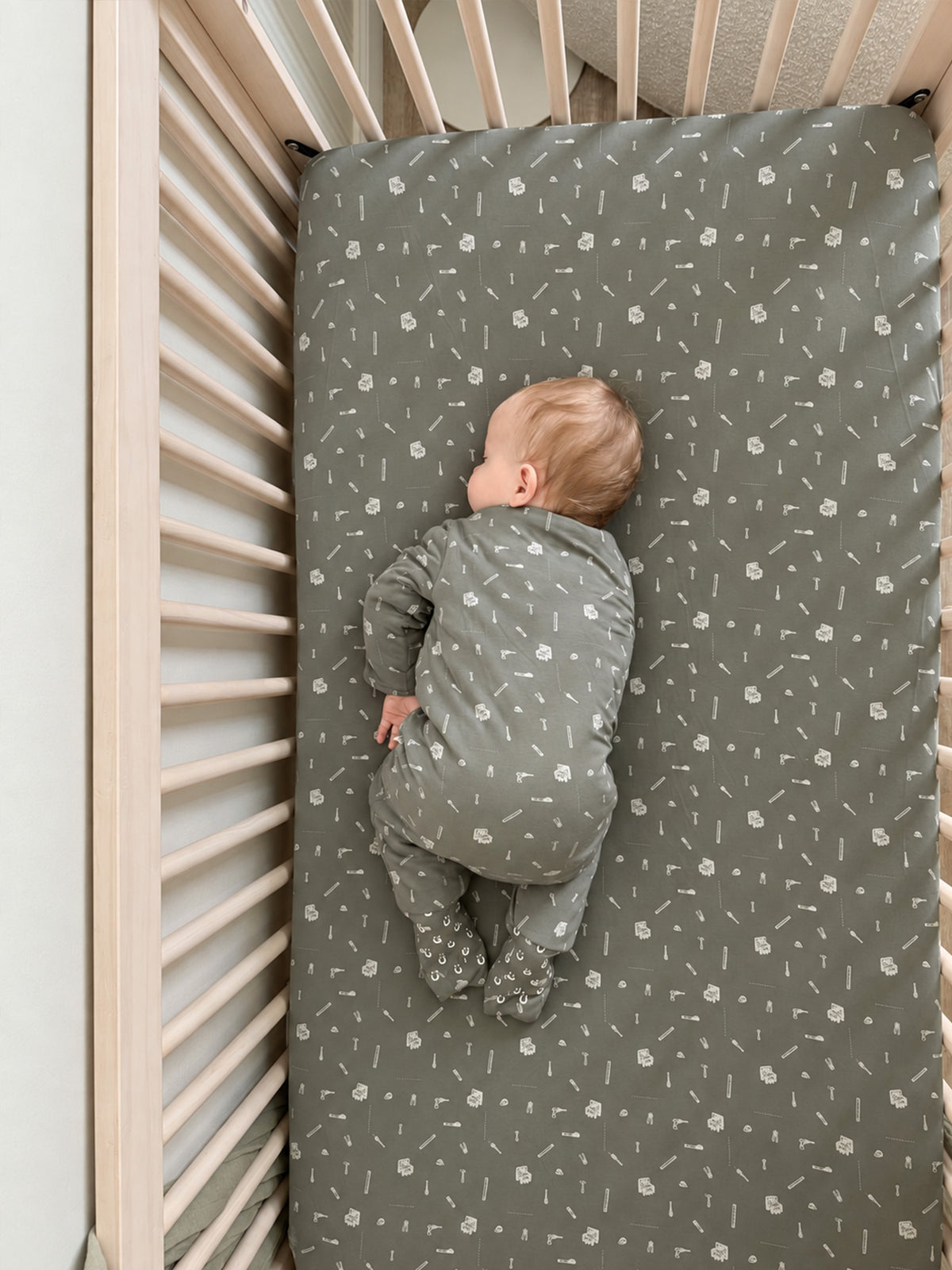 Grey crib sheet with white tool pattern, baby's back against mattress