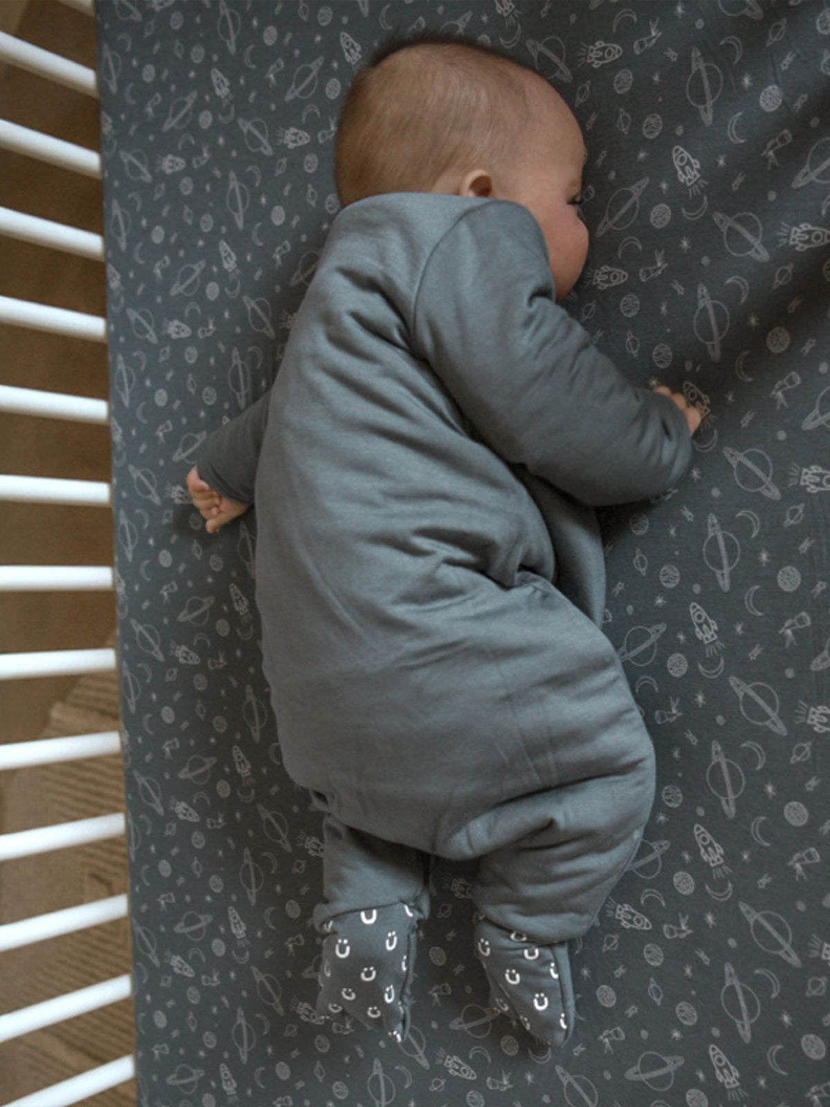 Gray long-sleeve sleep sack with zip-front and footed legs, turned away.