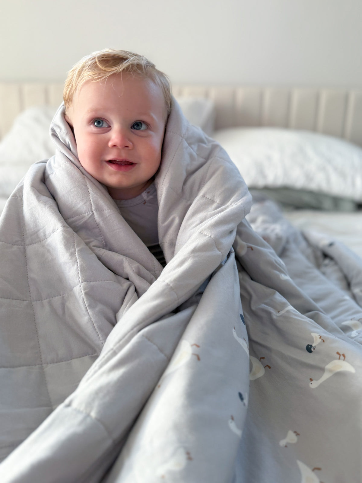 Light gray quilted baby blanket with small goose pattern, pulled around child