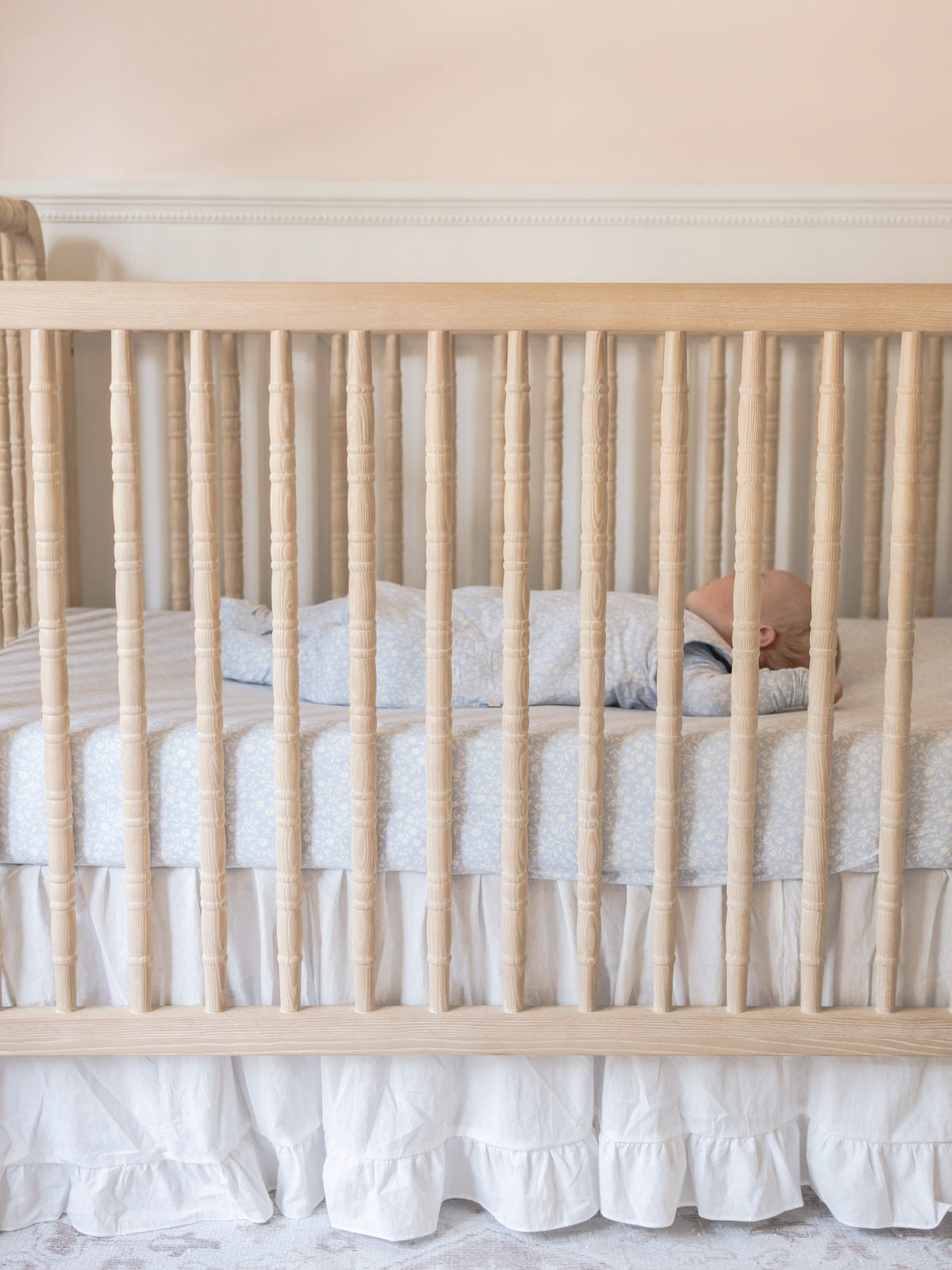 Light blue fitted crib sheet with white floral pattern, ruffled edge along the crib rail