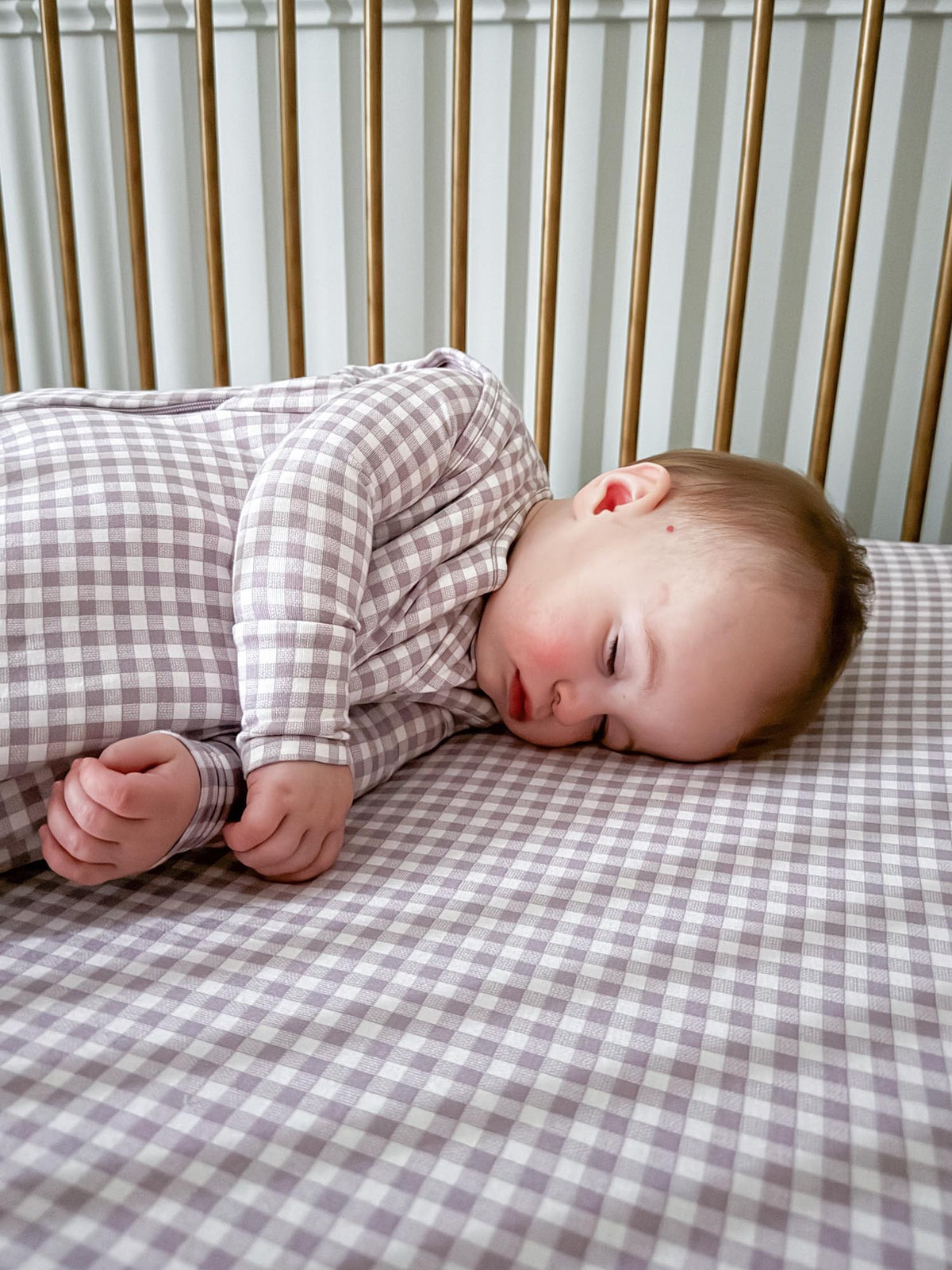 Crib sheet with light purple and white gingham pattern, baby lying on side