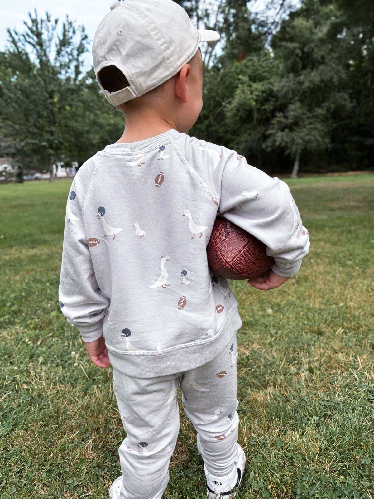 Kids fleece sweatsuit with duck and football print, toddler standing holding a football