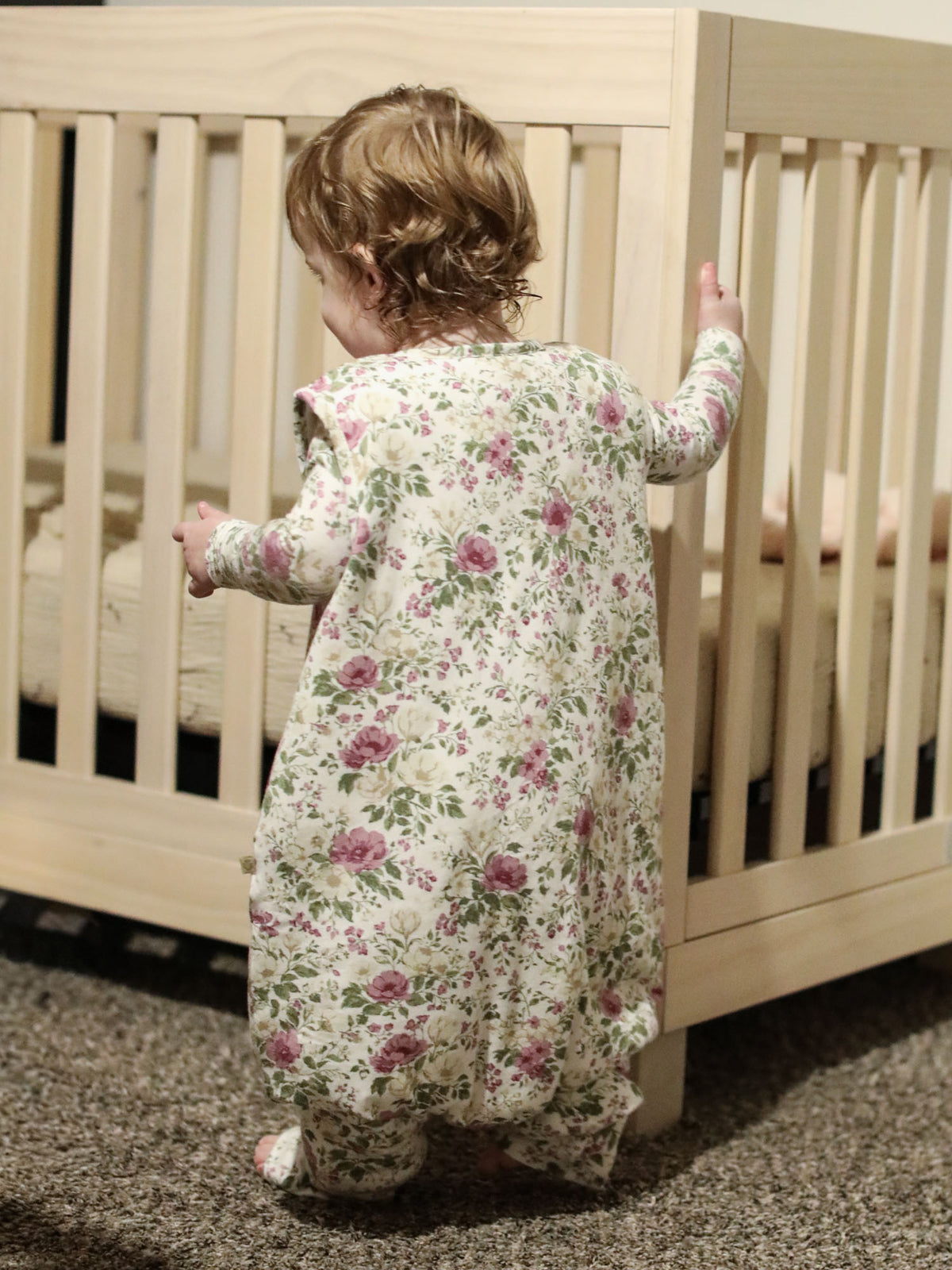 Back view of floral zip-front footed sleep sack, cream with purple flower print