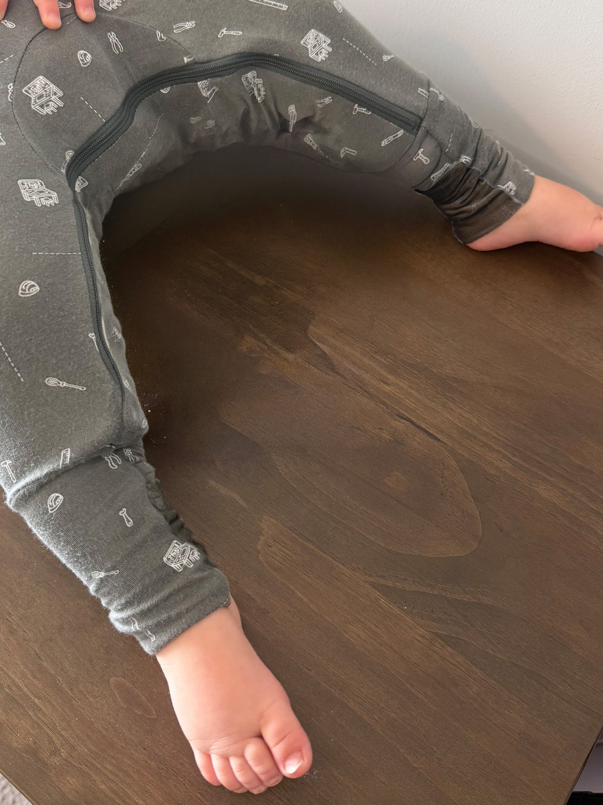 Convertible dark gray pajama with white tool icons, bare feet on wooden floor