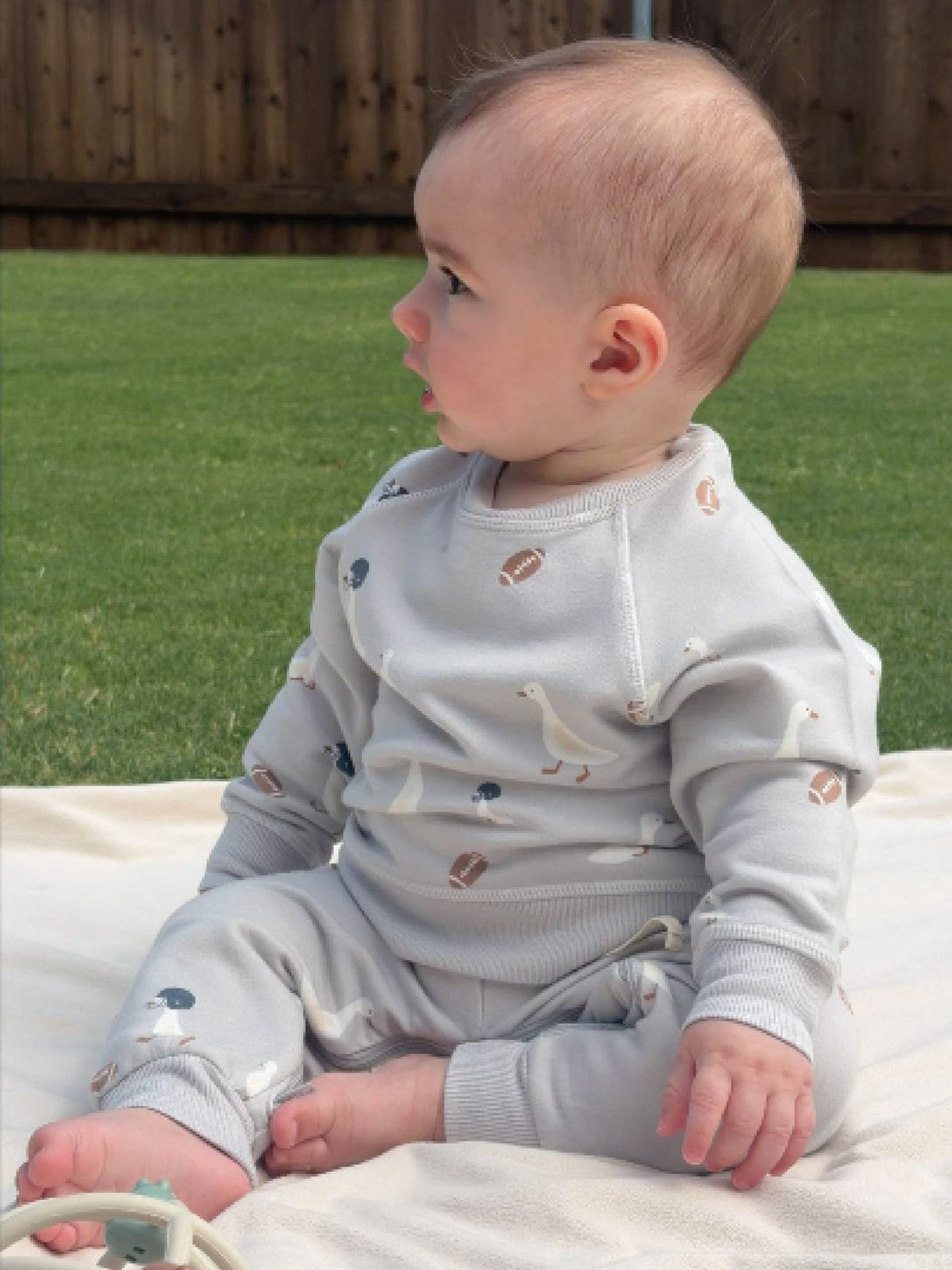 Kids fleece sweatsuit in light gray with duck and football print, relaxed seated toddler