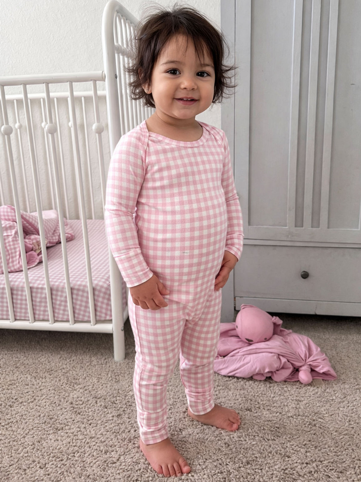 Pink gingham baby pajama set with long sleeves and footed legs, standing pose